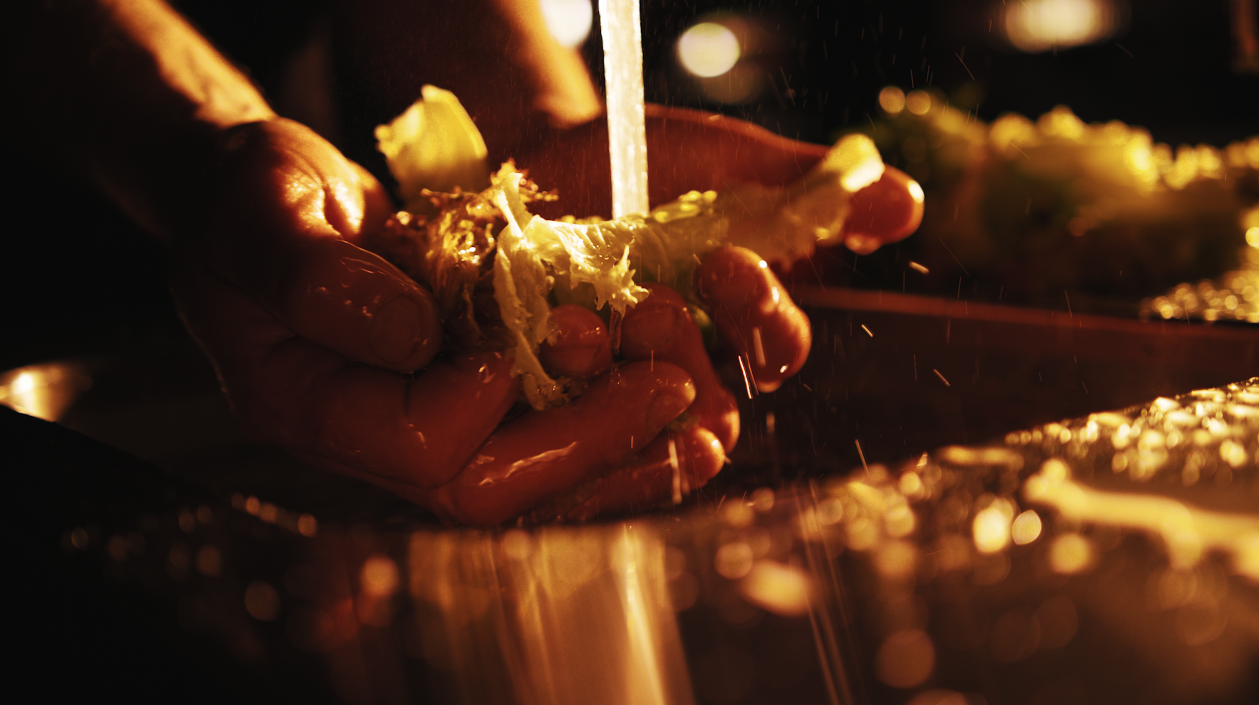 Close-up of hands washing grapes, with water and bubbles visible, illuminated by warm light.