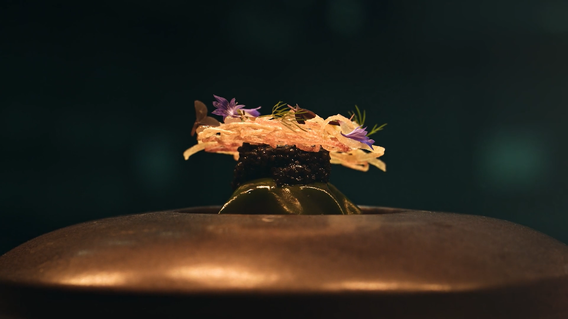 Elegant gourmet dish with layered ingredients, garnished with purple flowers, served on a copper plate.