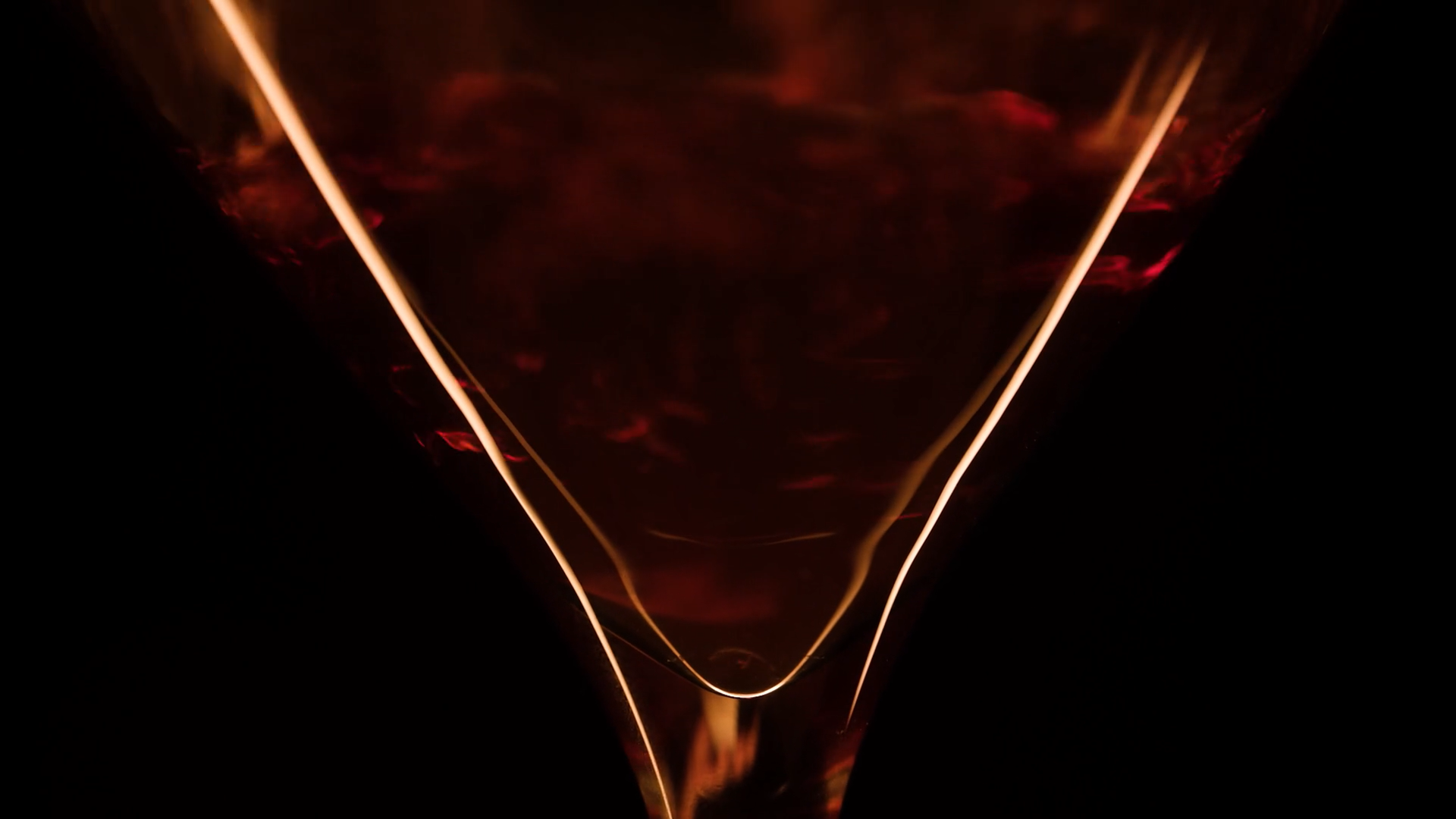 Close-up of a glass with a dark liquid, illuminated by light reflecting off the surface with swirling patterns.