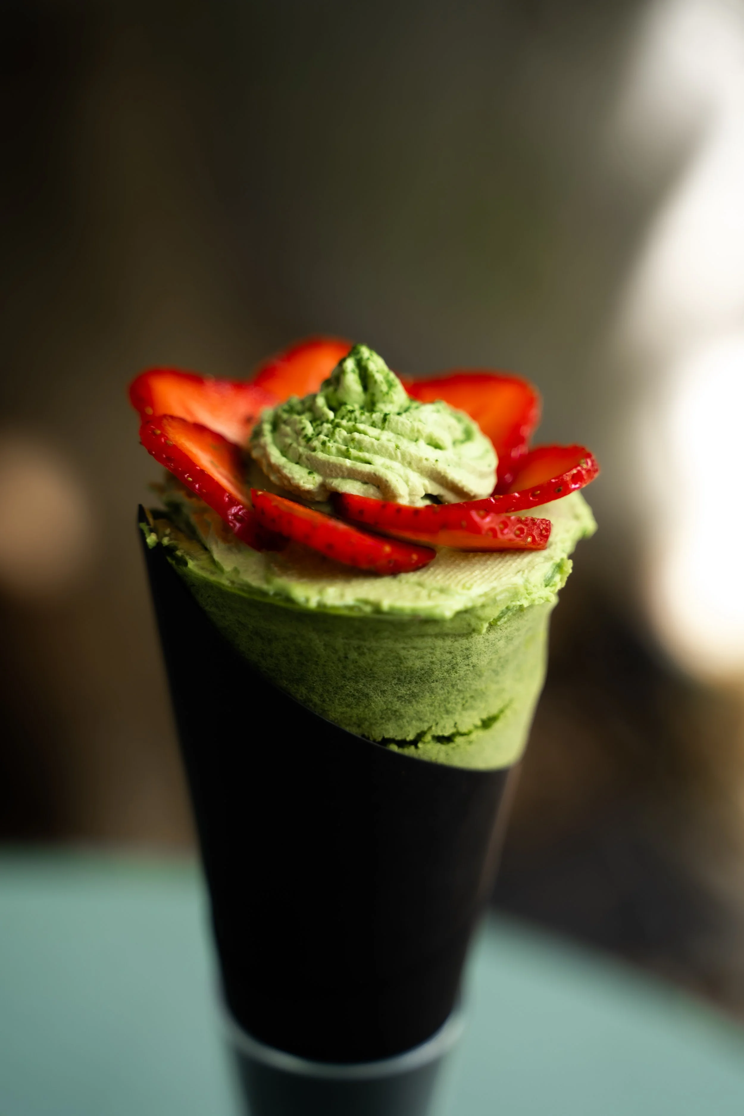 A matcha green tea ice cream cone decorated with sliced strawberries on top.