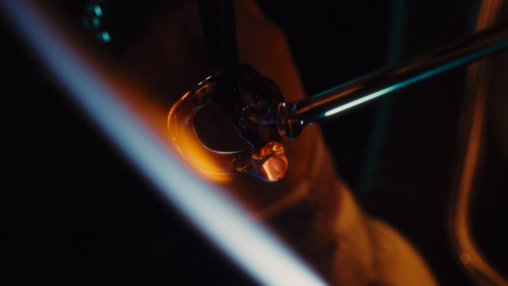 A close-up of a glass object being heated with a torch, creating a glow and melting the glass, in a dark environment.