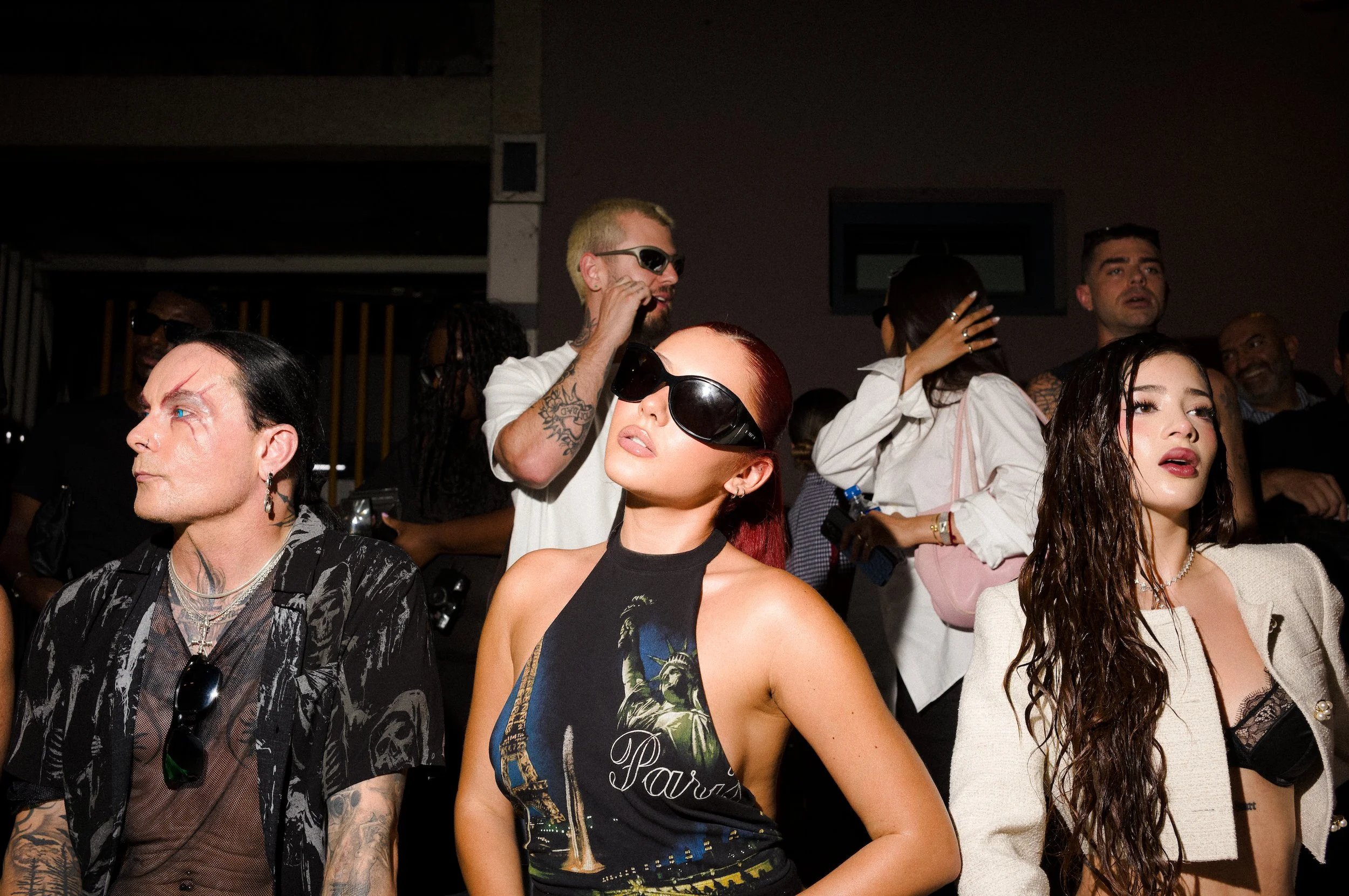 Atiana de la Hoya at the Vetements show for Paris fashiion week, wearing sunglasses, sitting in a dimly lit indoor setting.