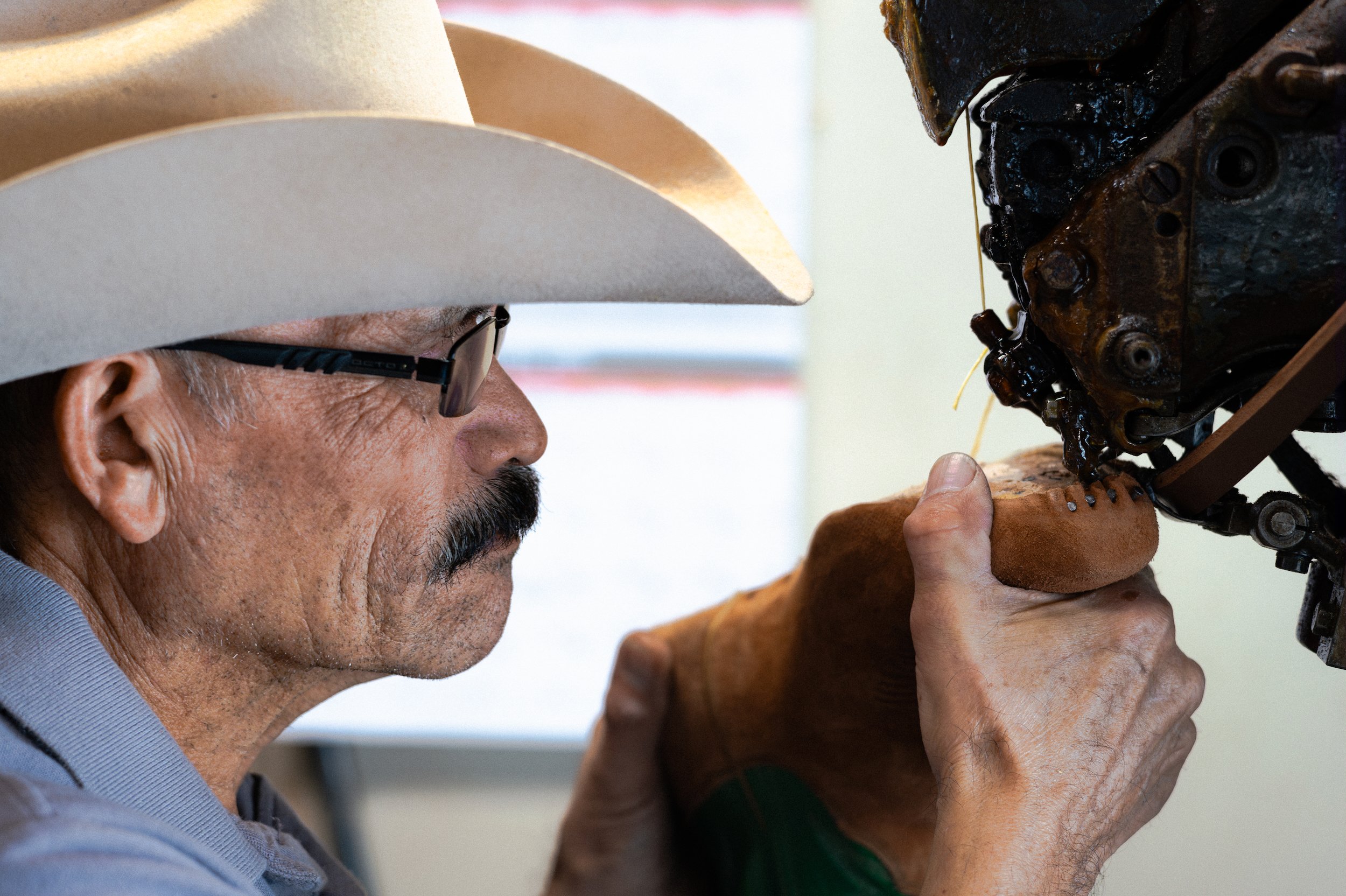 A man wearing a cowboy hat and glasses working on a pair of Boots.