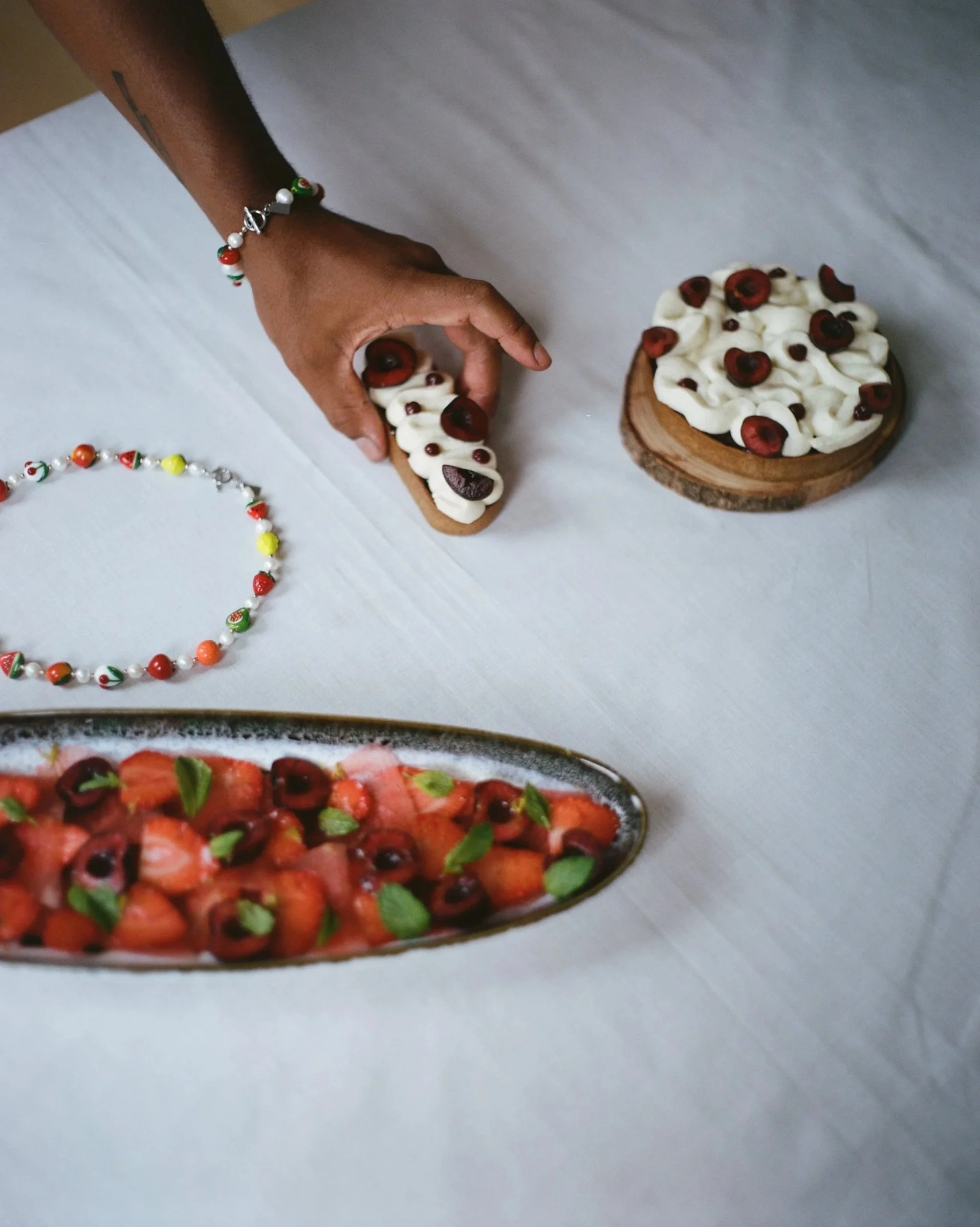 A person placing decorated cookies on a white table next to a plate of strawberry and berry dessert garnished with mint leaves.