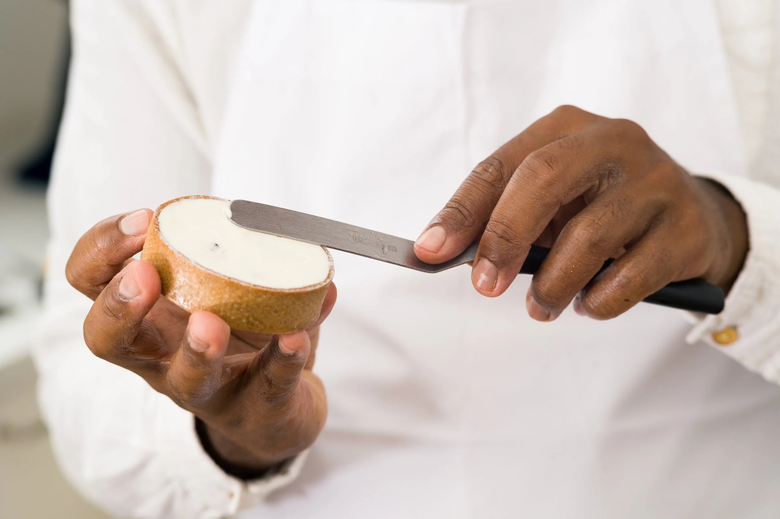 A chef spreading white frosting on a round pastry using a metal spatula.
