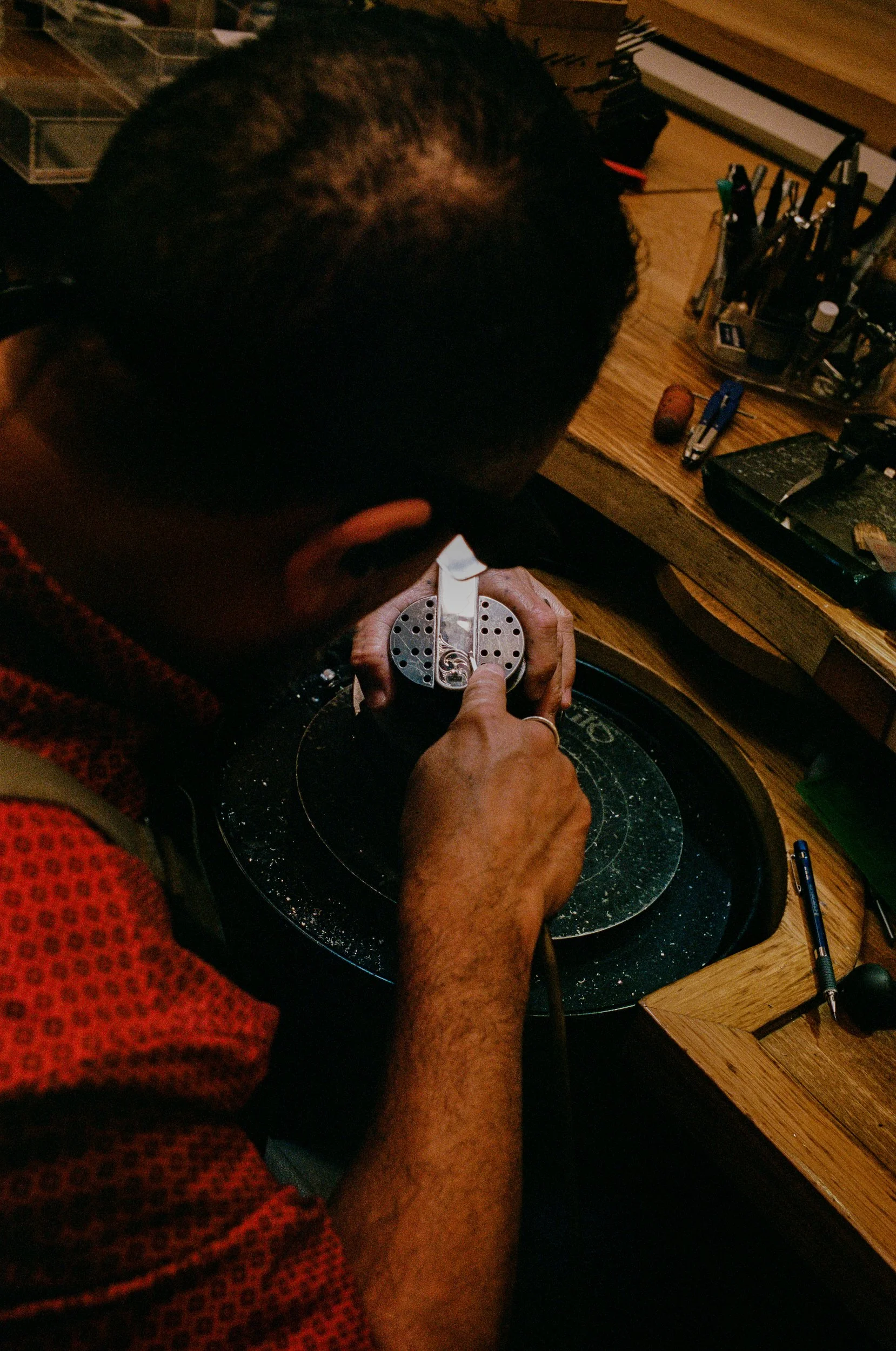 At Clint Orms Silver workshop, a person working on a piece of silver with a small drill or polishing tool, surrounded by various tools on a wooden workspace.
