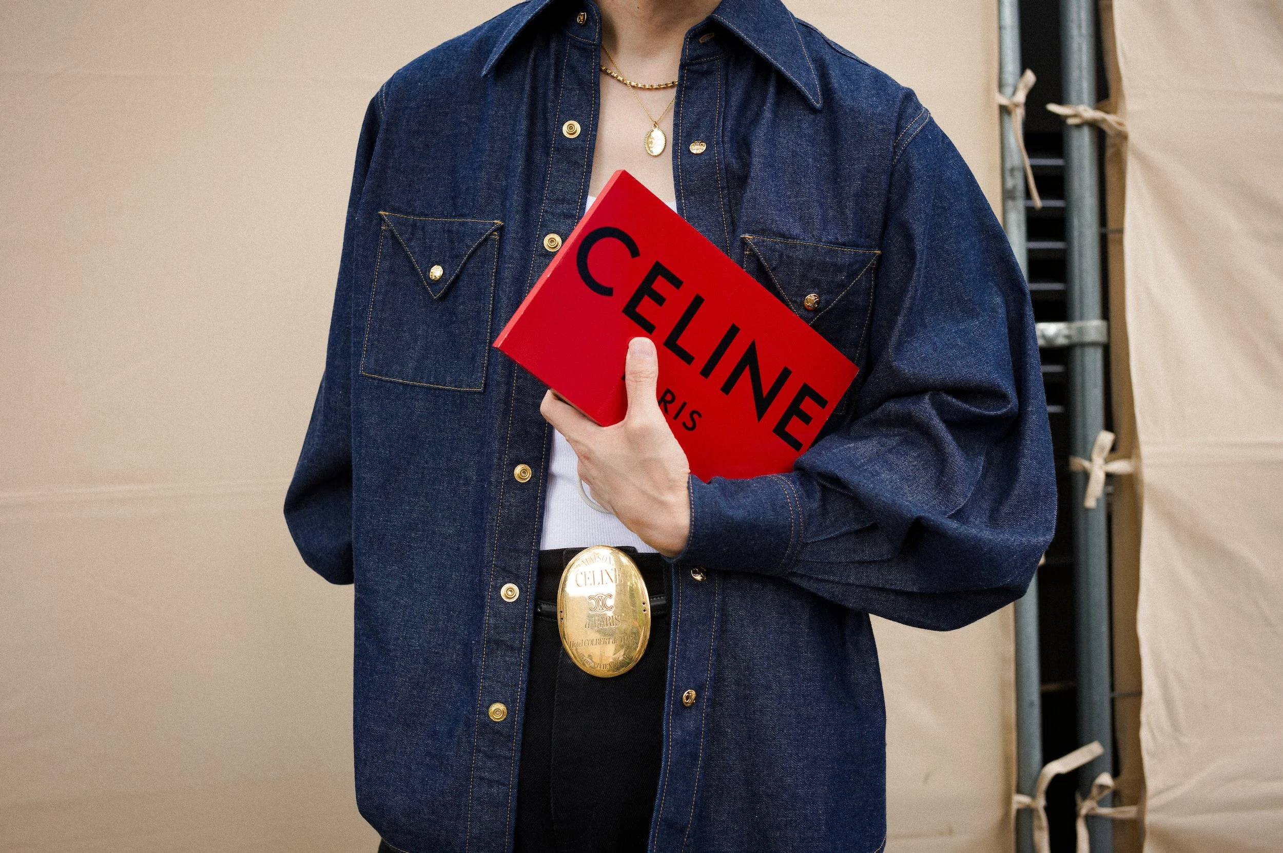 At Paris Fashion week; Person wearing a dark blue denim jacket and holding a red sign that says 'CELINE PARIS'.