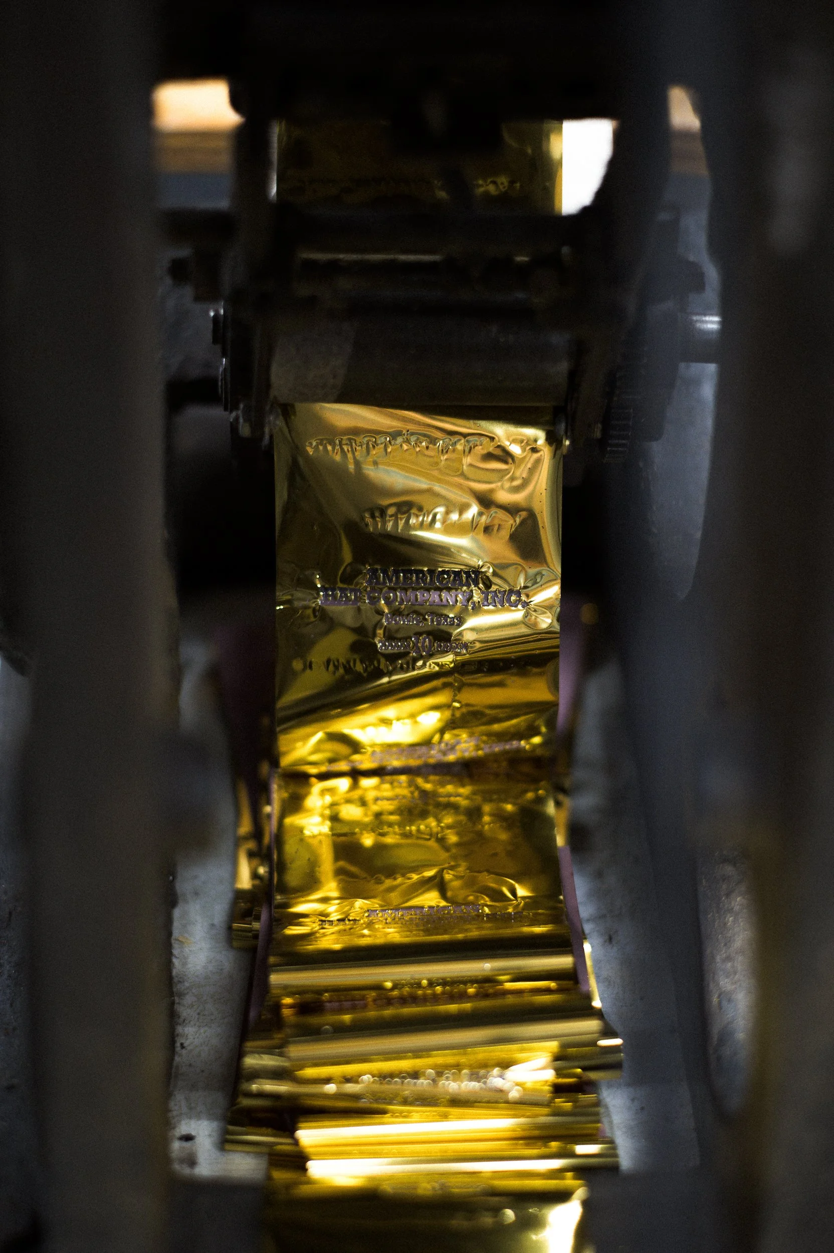 Close-up shot of the metallic gold foil imprint that are printed on the inner lining, inside a machine, with machinery parts on either side.
