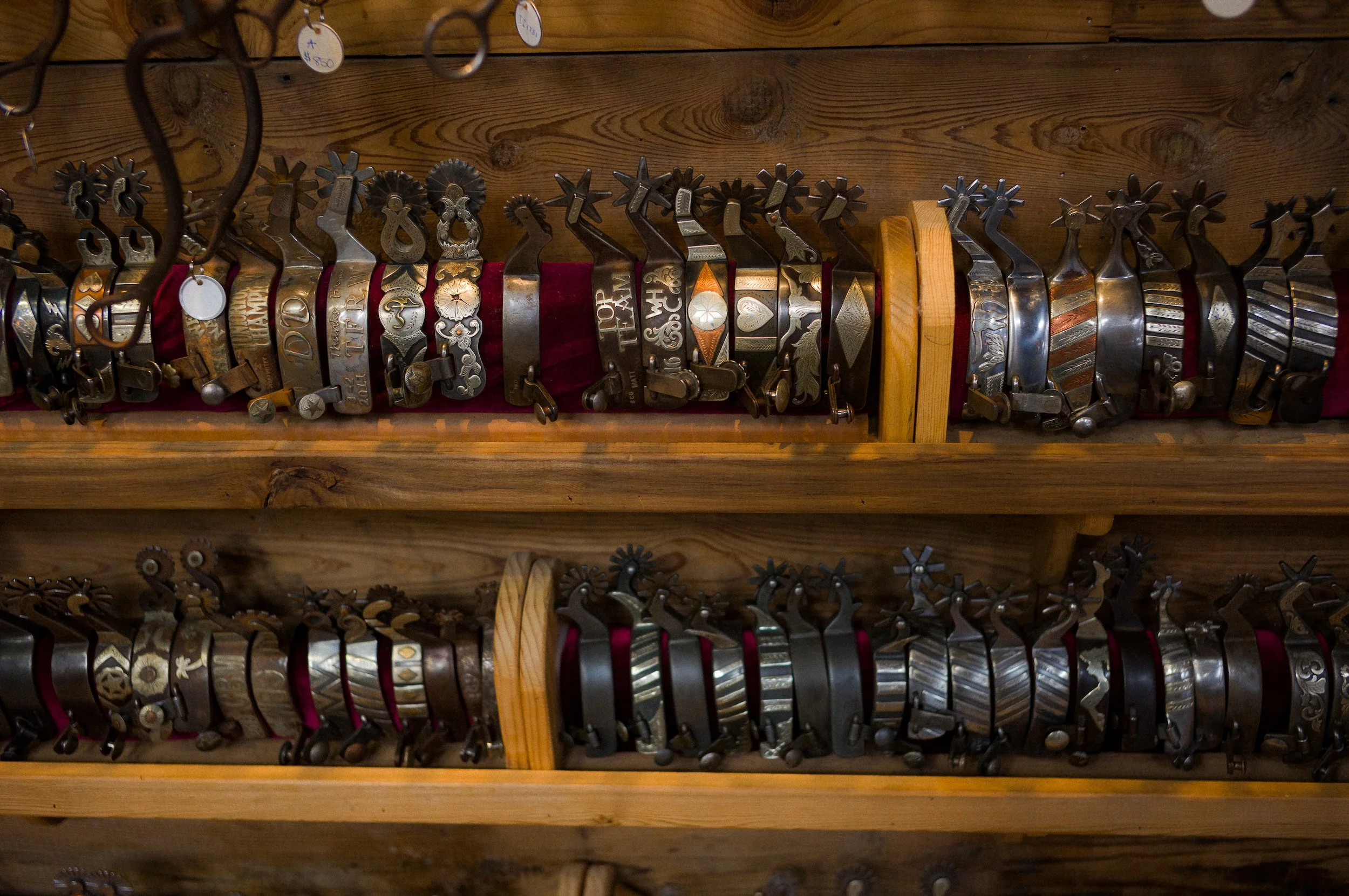 Display of various decorative metal Spurs hanging on wooden shelves.