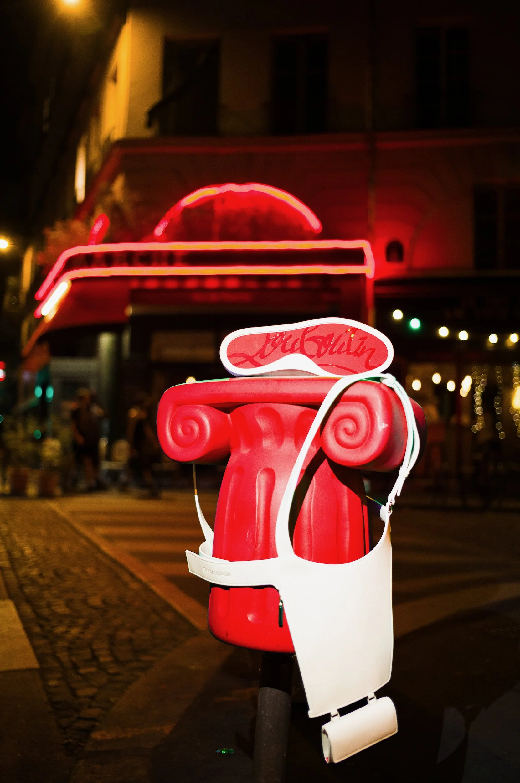 A redstool with a white harness and a neon pink and red sign above it, mounted on a pole on a city sidewalk at night.