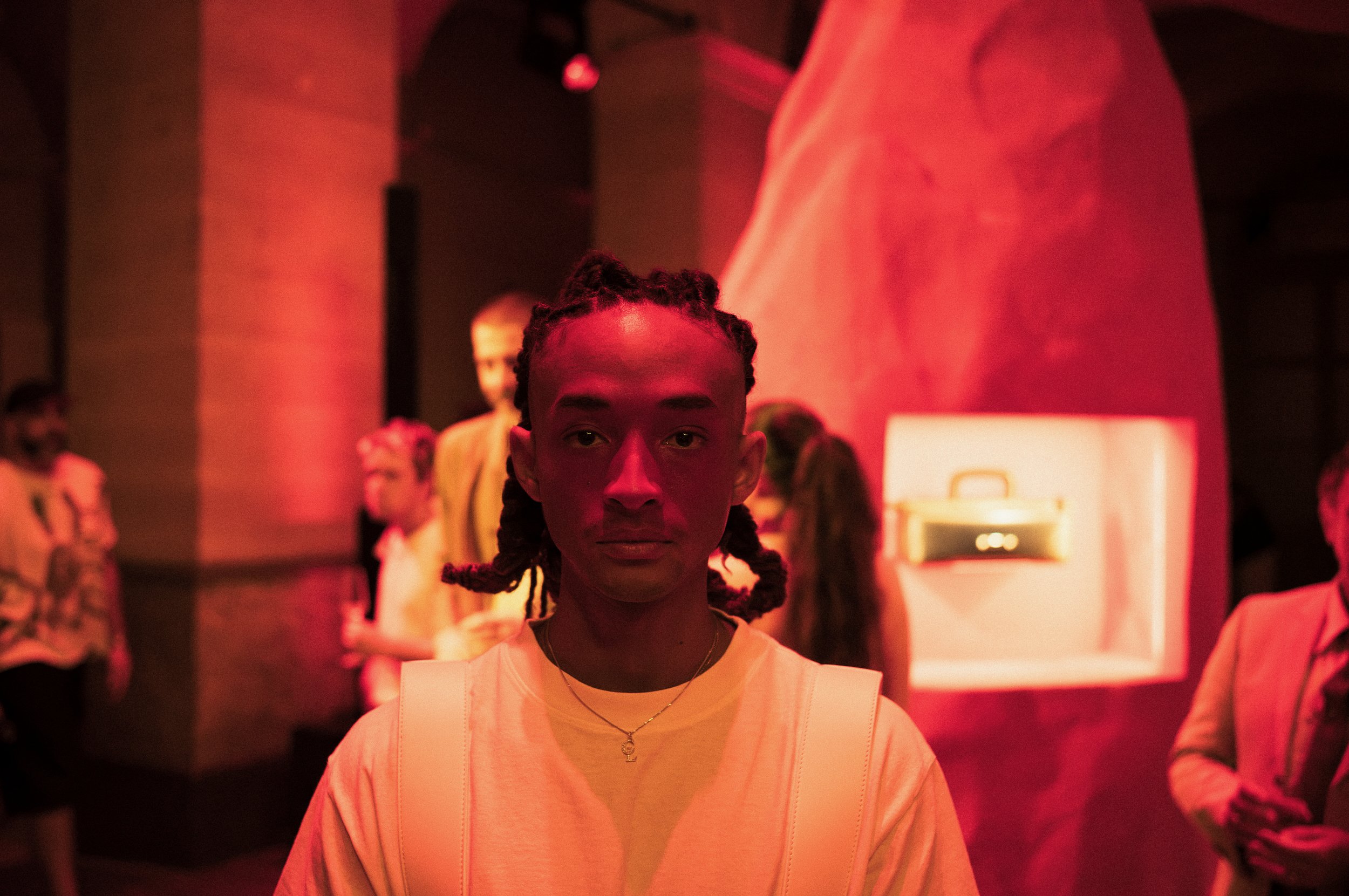 Jayden Smith, standing in a dimly lit room with red lighting, with other people in the background.