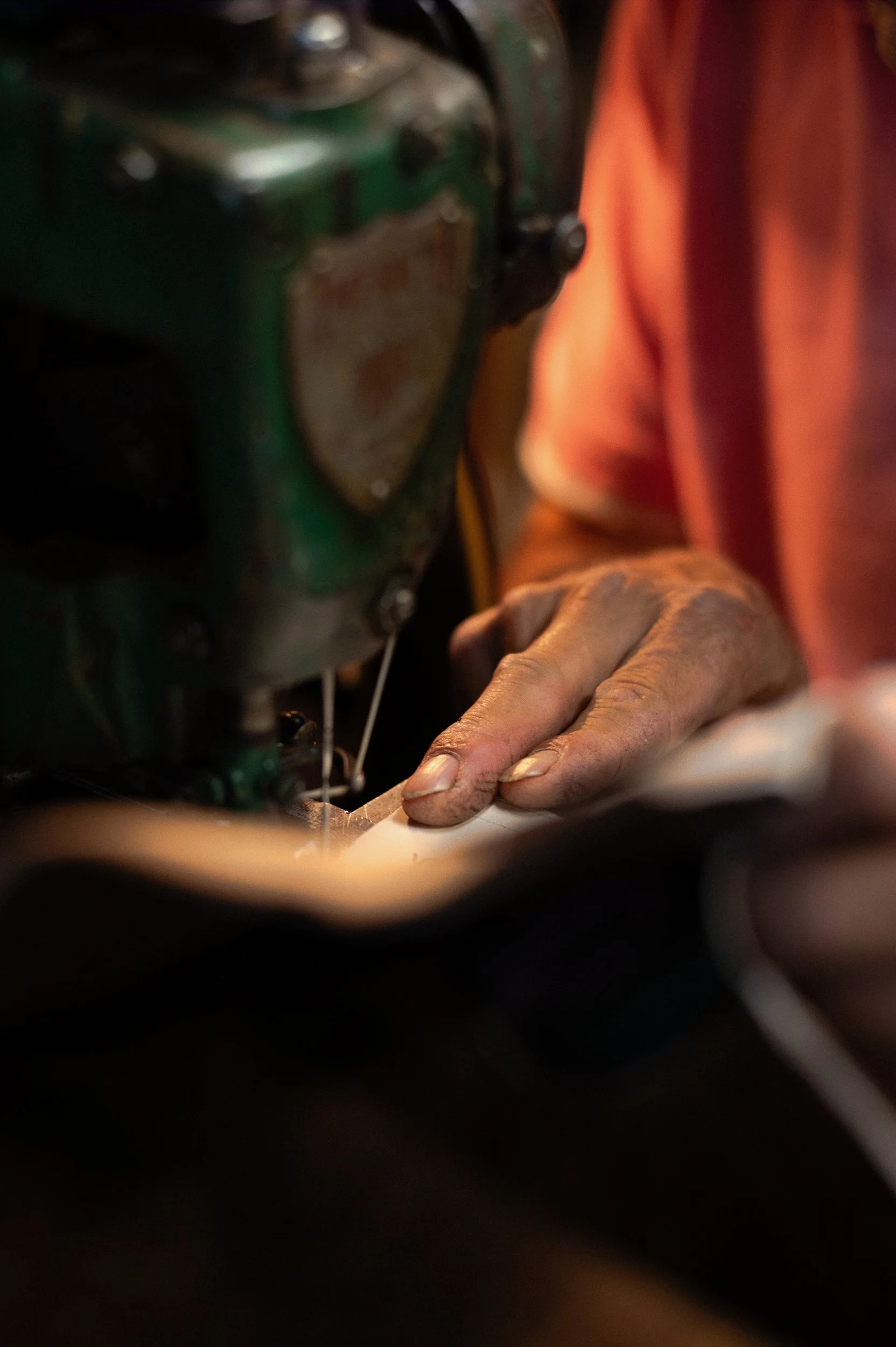 A person's hand working on a machine to make cowboy boots, with parts of the machinery visible in the background.