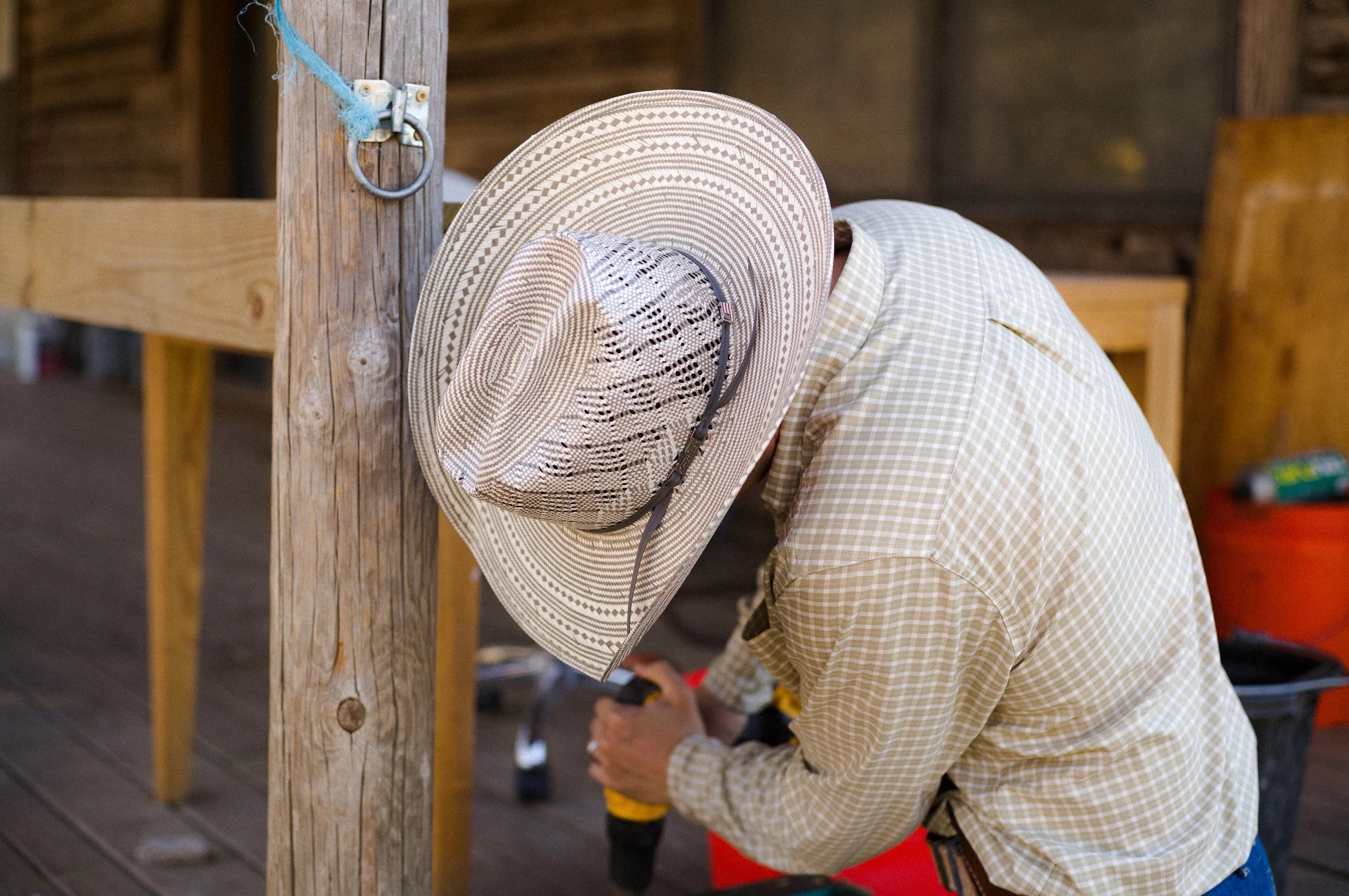 Cowboy with a straw hat leaning over a wooden pole on a porch or outdoor deck.