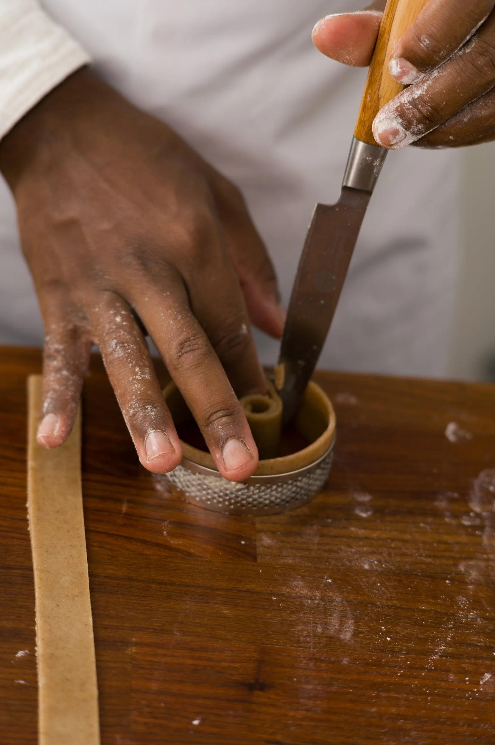 Close-up of hands dusted with flour making pasta using a pasta cutter and a mold on a wooden surface.
