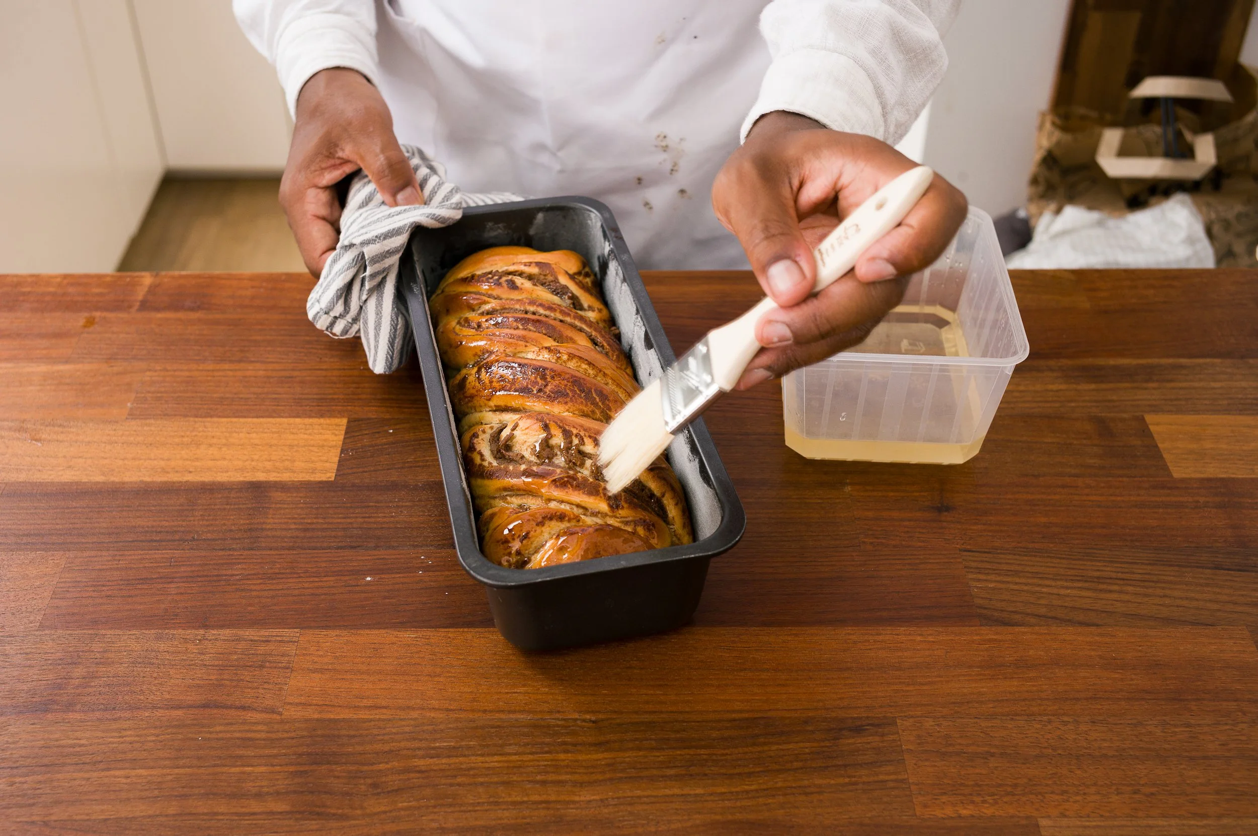 A chef slicing a freshly baked bread loaf in a baking pan on a wooden table.