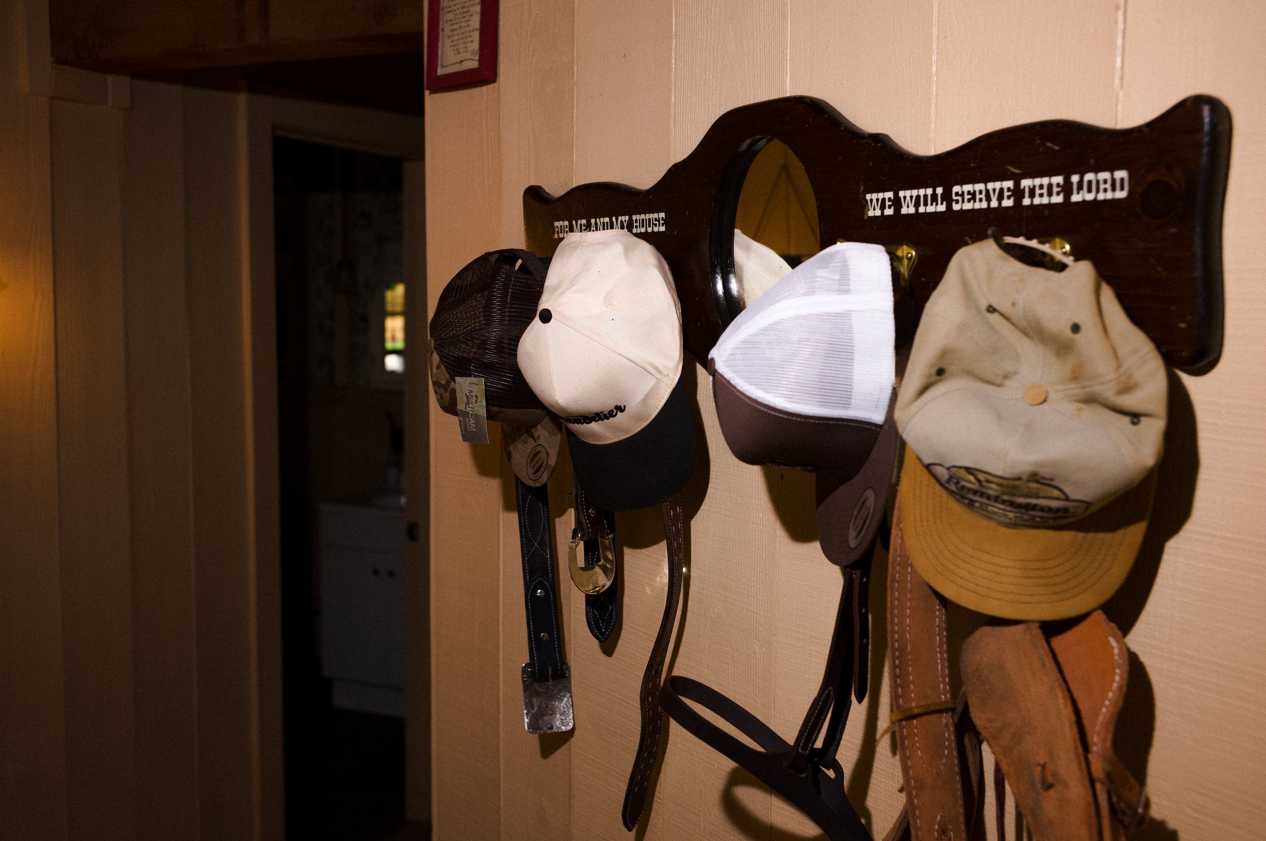 Hats hanging on a wooden rack with the inscription 'For me and my house, we will serve the Lord' in a room with beige walls.