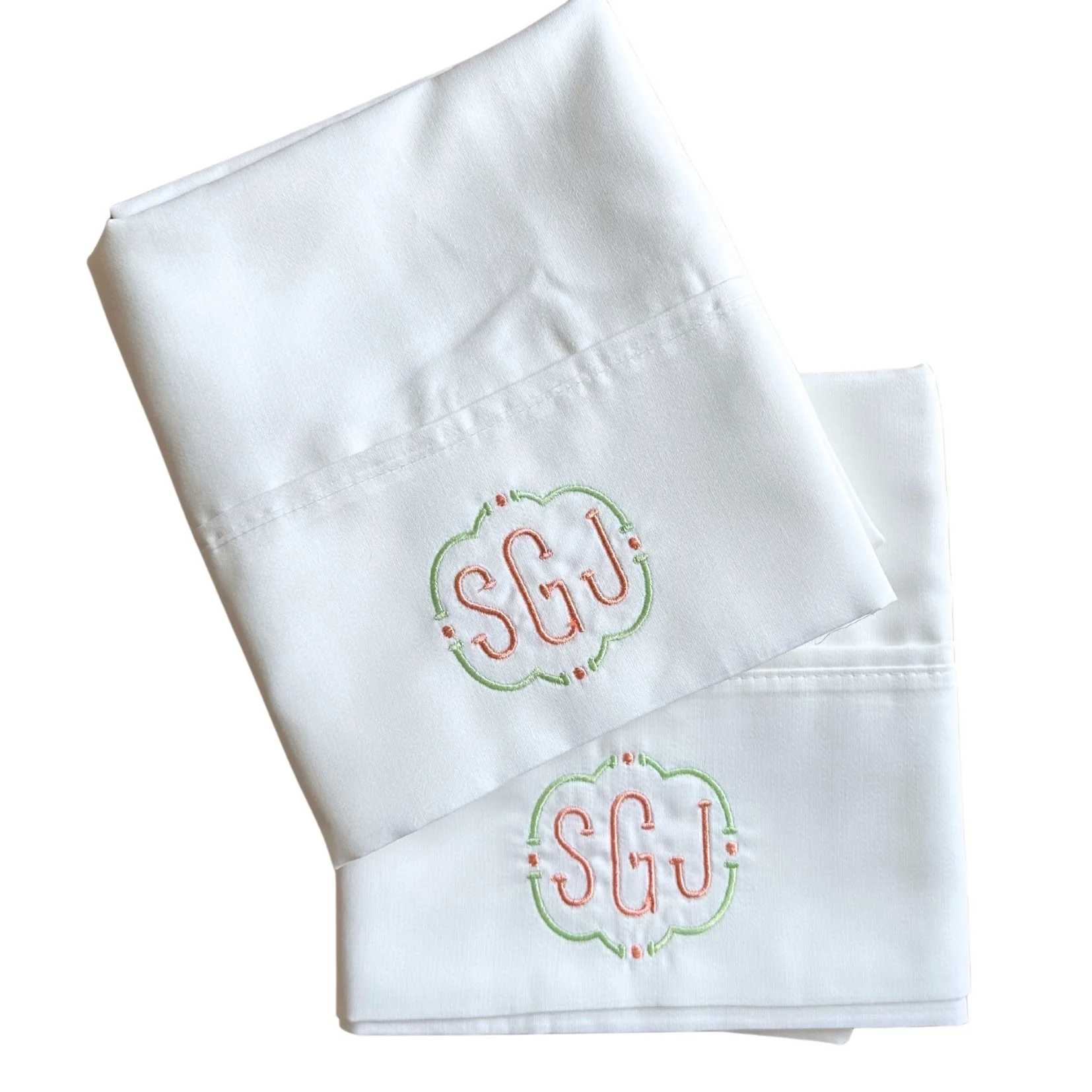 Two white cloth napkins with embroidered monograms 'SGU' in pink, surrounded by a green and pink decorative border.
