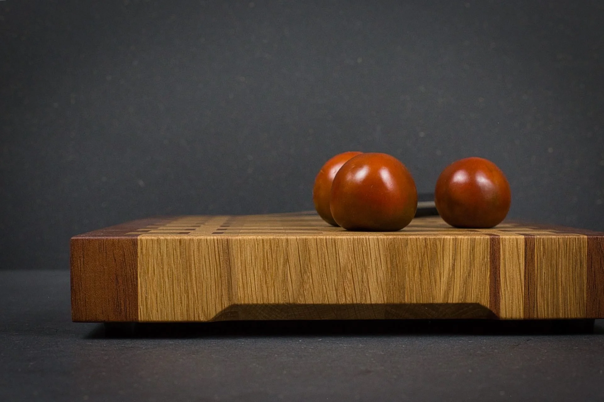 Vue rapprochée de la tranche d'une planche à découper en bois de bout, alternance chêne et acajou, avec tomates