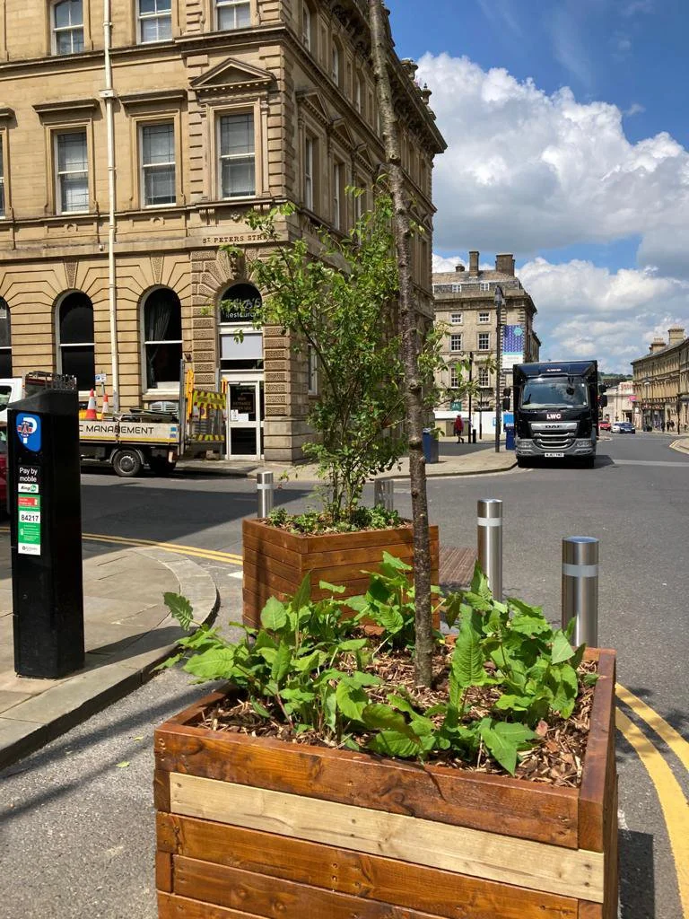 Square wooden planters on the street corner. https://www.paxman-landscapes.com/huddersfield-high-street-planters/