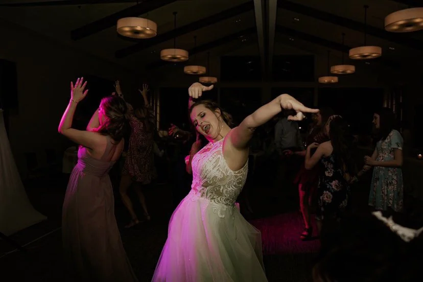 Woman in a white dress dancing with joy at a party, surrounded by other people dancing.