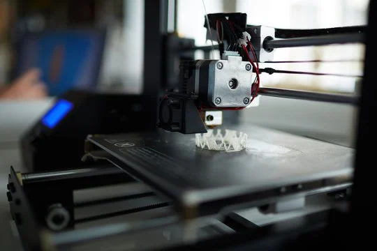 Close-up of a 3D printer in operation, printing a small object with white filament.