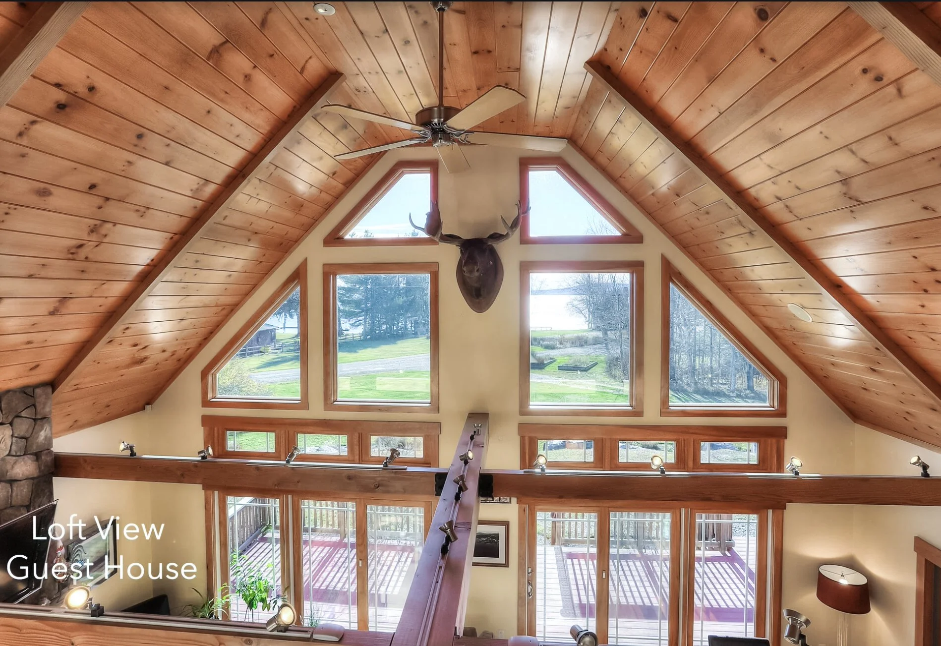 View of a spacious living area inside a guest house with a vaulted wooden ceiling, large triangular windows, and a mounted deer head on the wall.