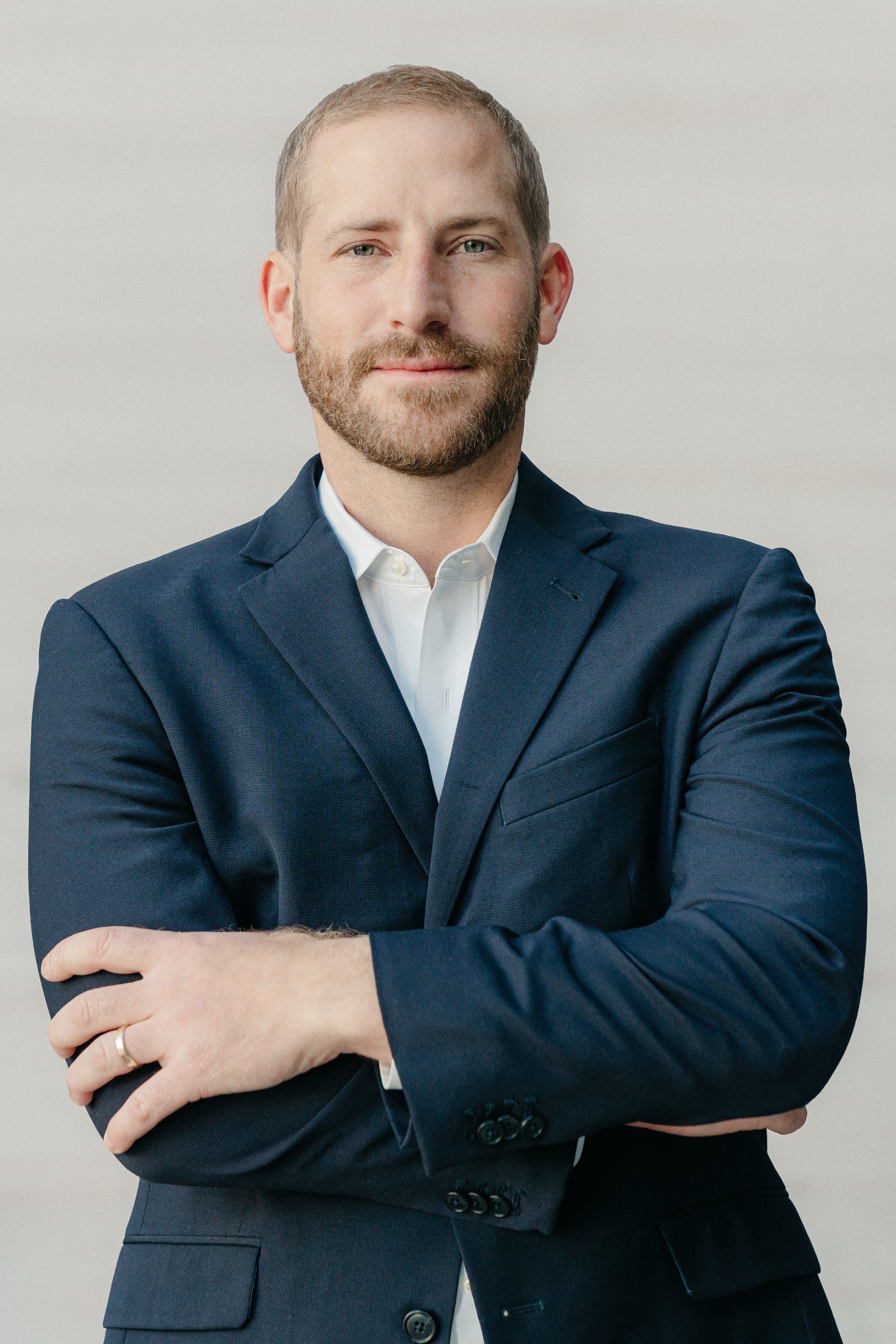 A professional man in a dark blue suit with a white shirt, arms crossed, looking confidently at the camera.