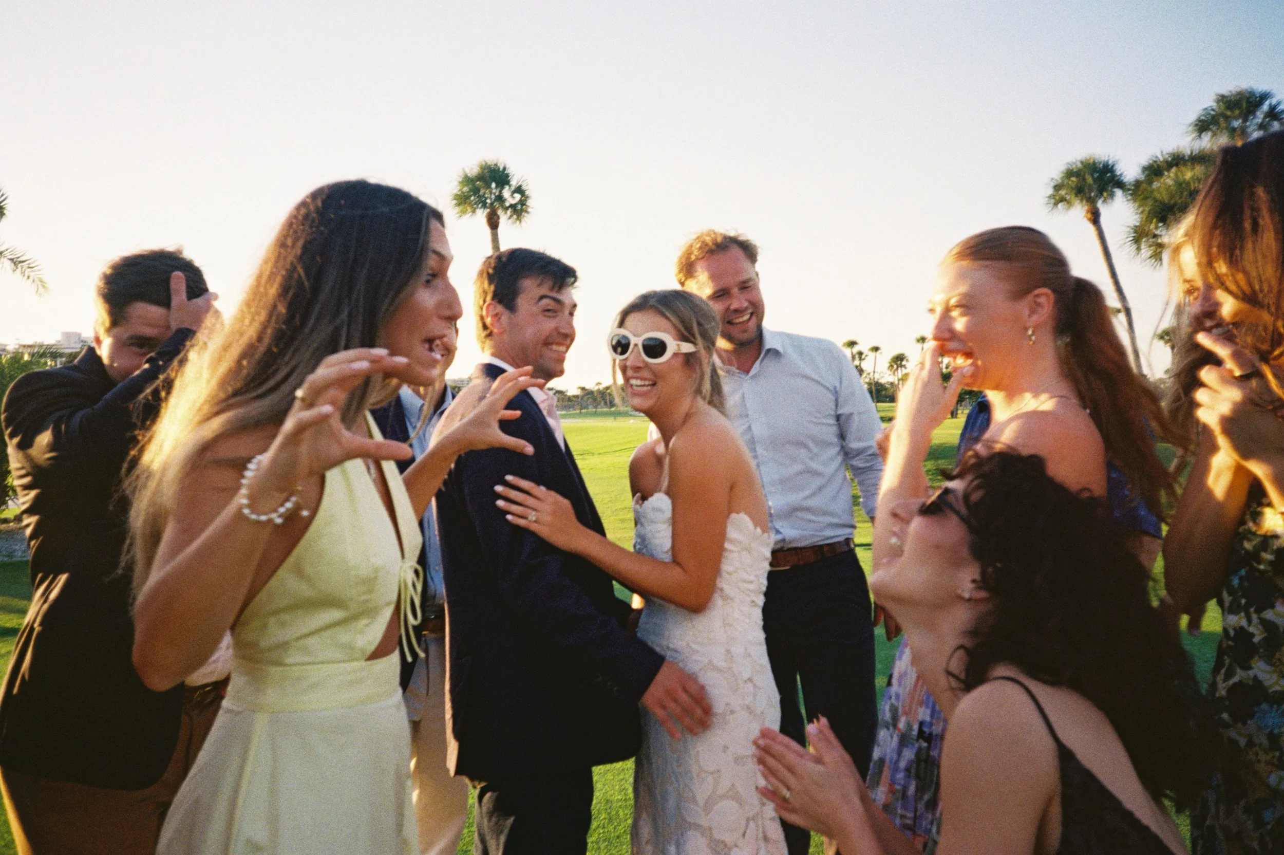 A group of people celebrating outdoors, some are laughing and talking, with a woman in a wedding dress in the center. Bridal Party, Celebration, LIZAEVEPHOTO, organic, candids