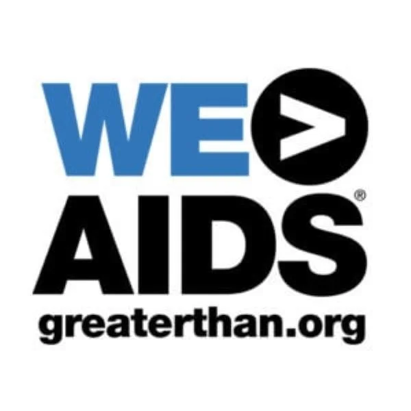 Logo for greaterthan.org featuring the words "WE" in blue, a black circle with a white greater-than symbol, and "AIDS" in black, promoting awareness and support for AIDS prevention.