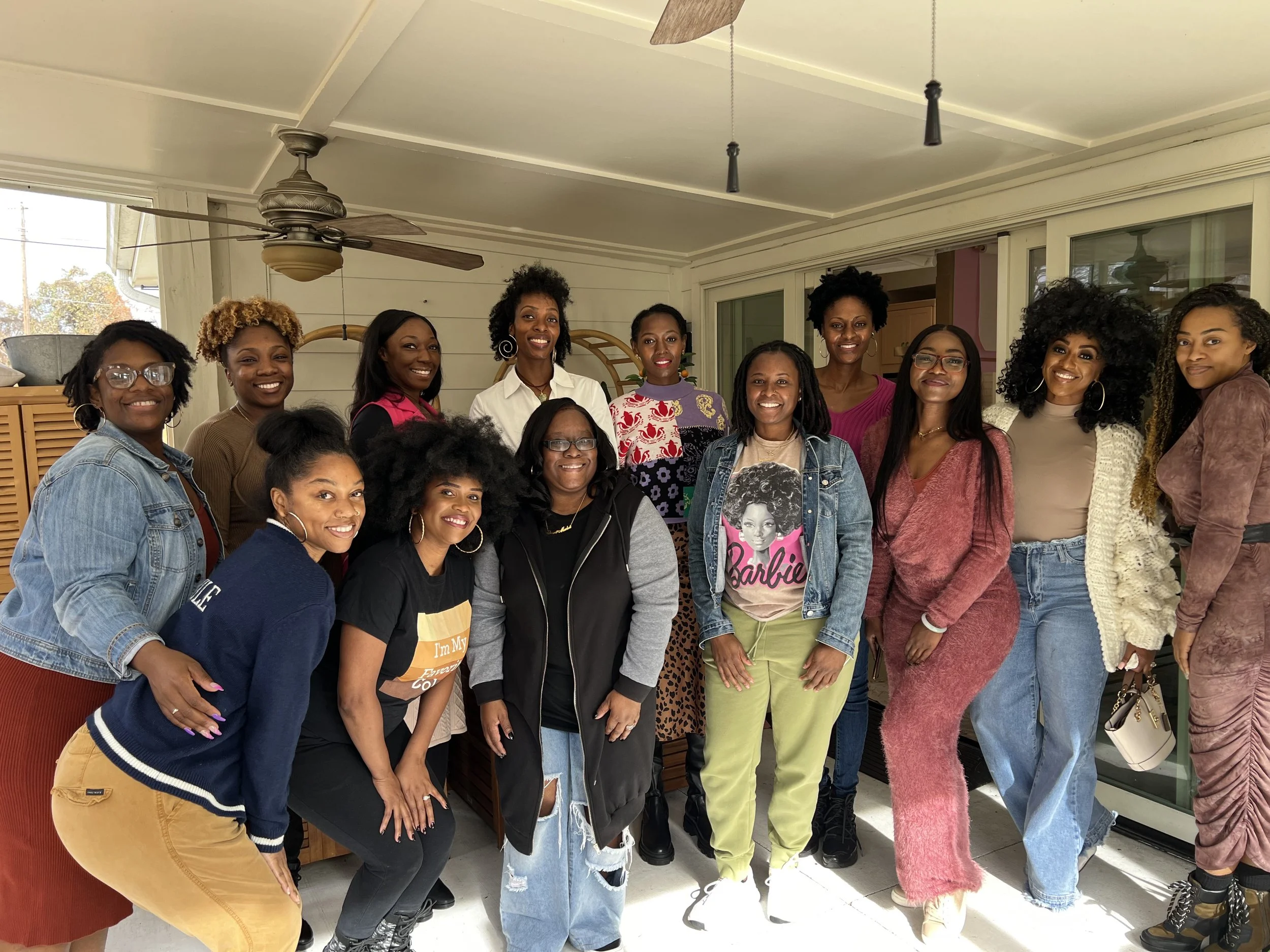 Group of 15 women posing indoors for a photo, smiling and standing close together.