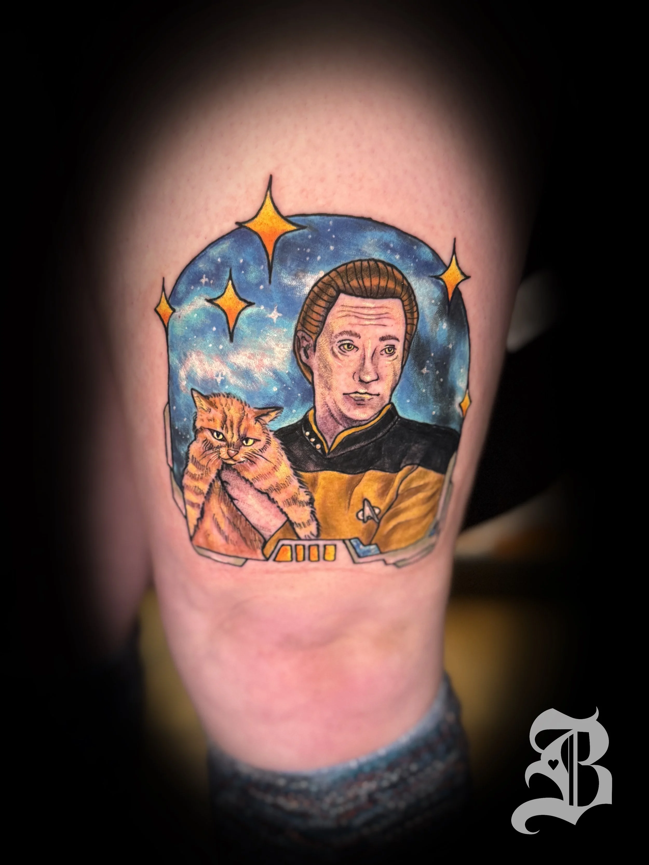 Tattoo of a Star Trek character in a yellow uniform holding a tabby cat, with a starry space background by Binx inks.