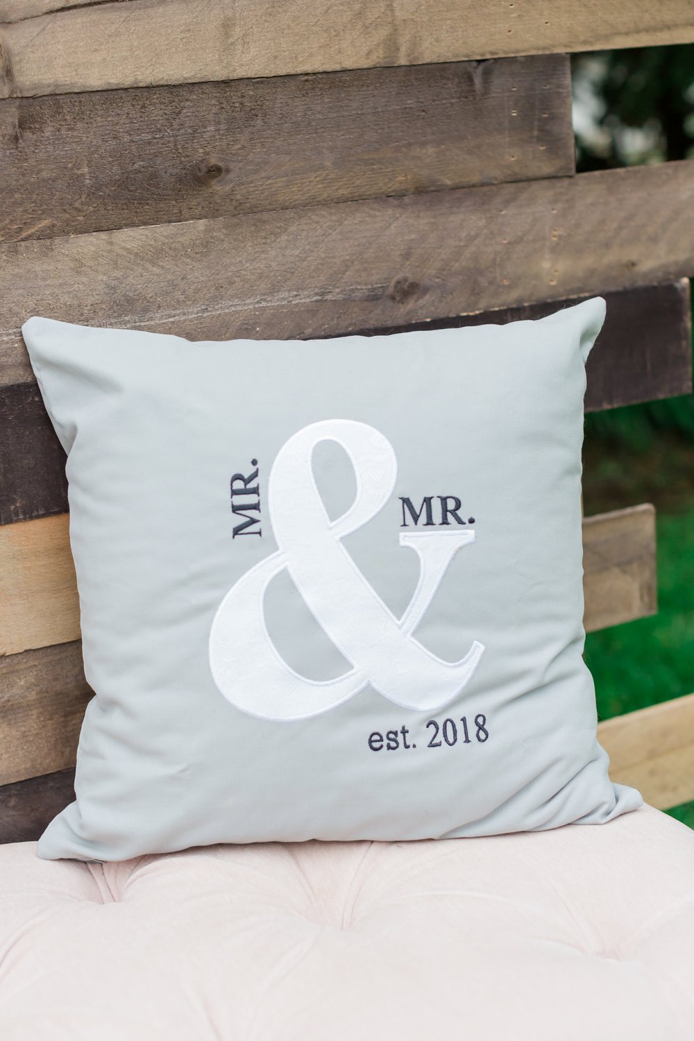  A pillow with embroidery that reads “Mr. &amp; Mr. est. 2018” 