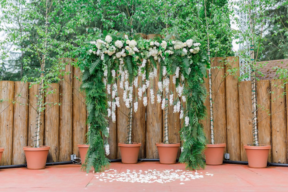  A wedding ceremony backdrop with abundant greenery and hanging white flowers. 