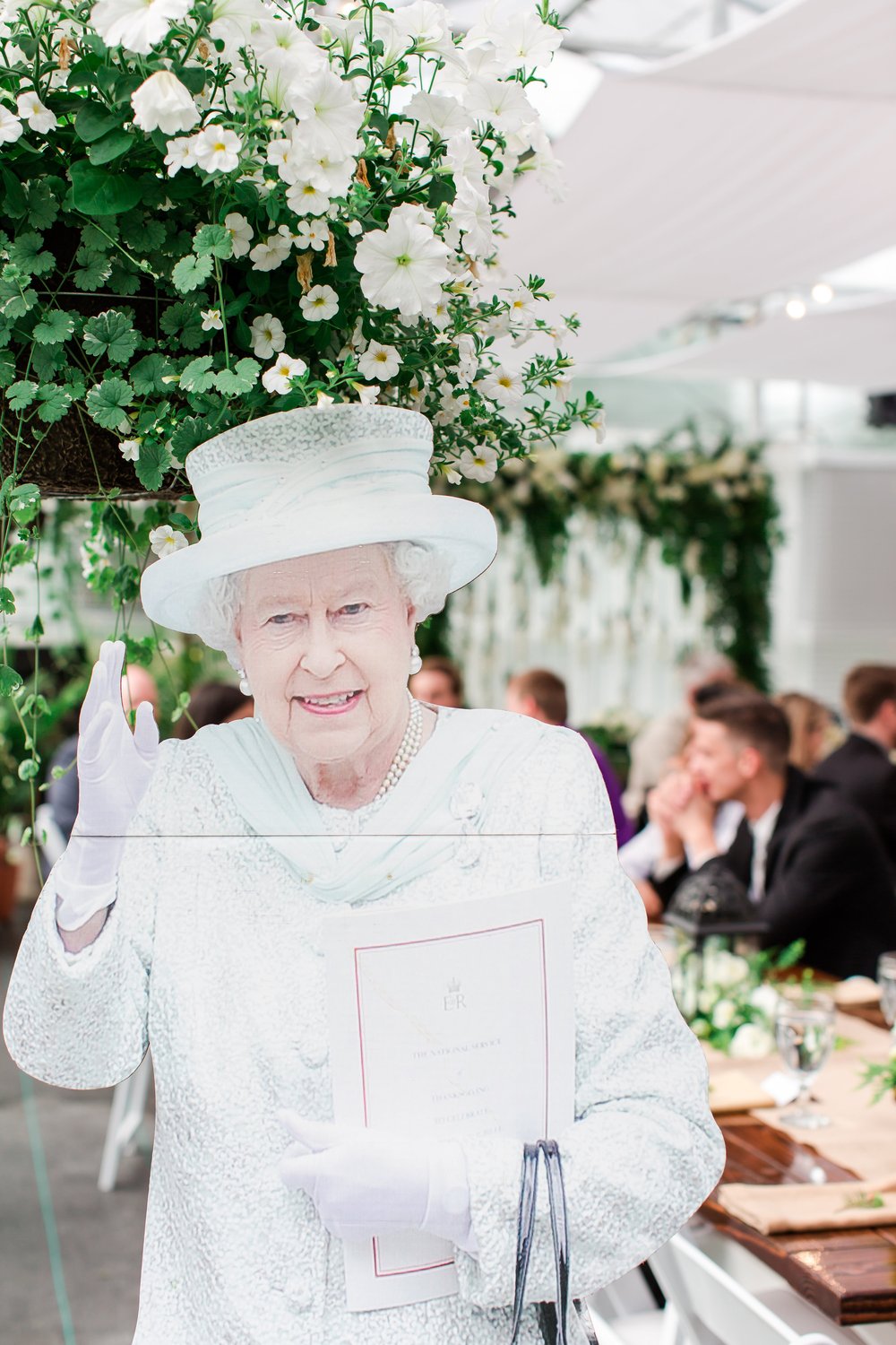  A cardboard cut out of Queen Elizabeth is posed with a wedding reception in the background 