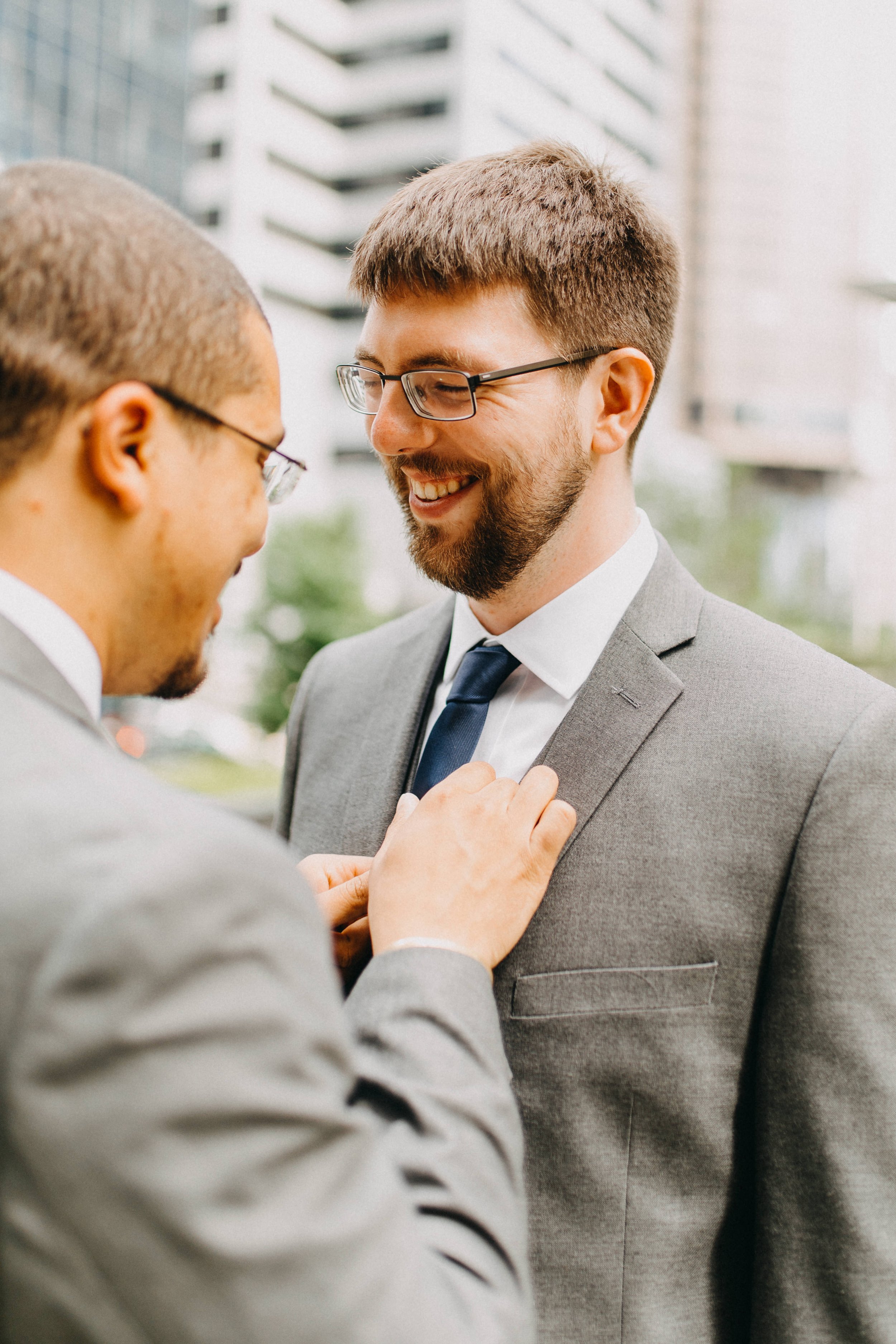  A groom is smiling while his future husband adjusts his tie. 