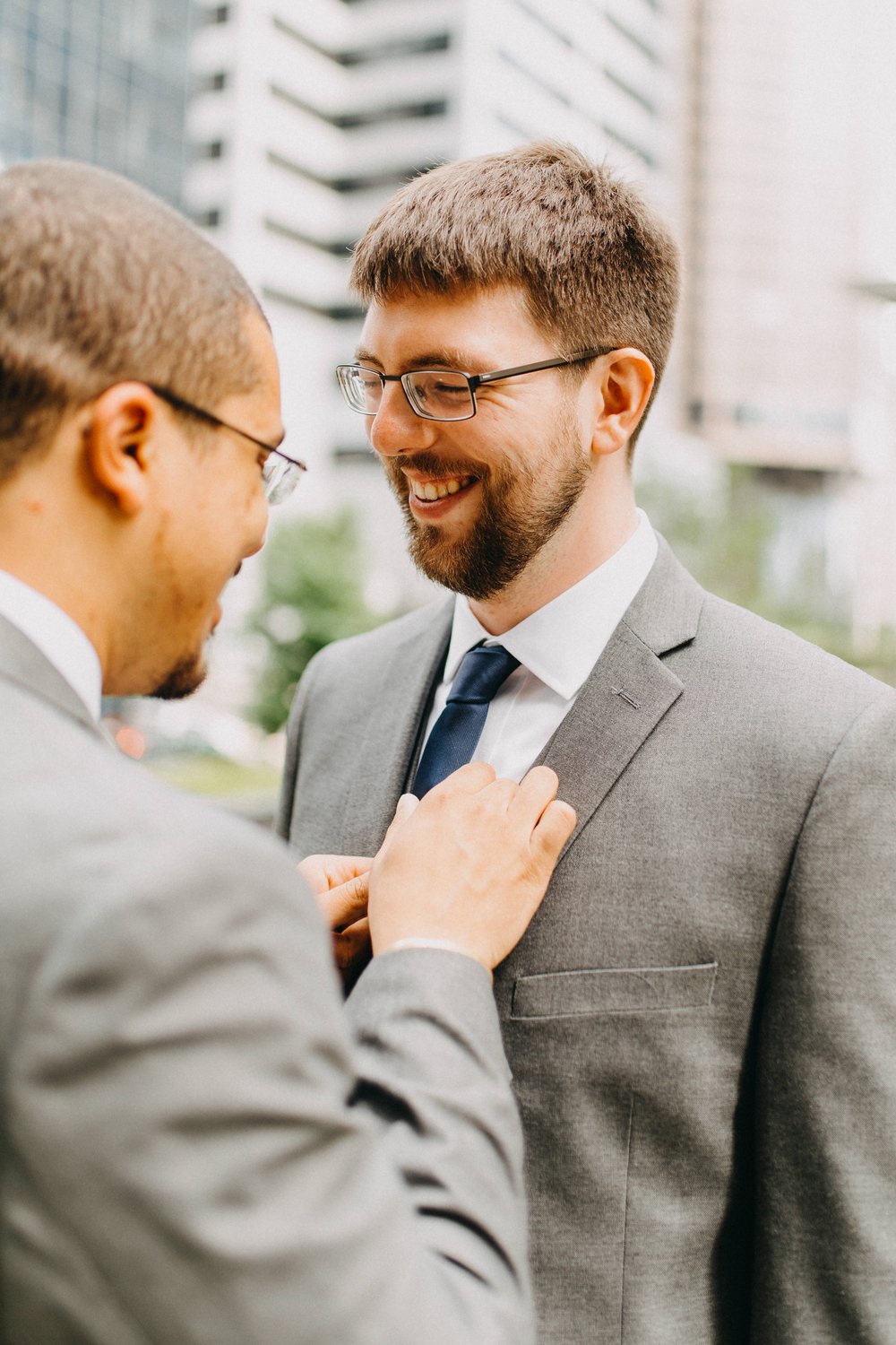  A groom is smiling while his future husband adjusts his tie. 