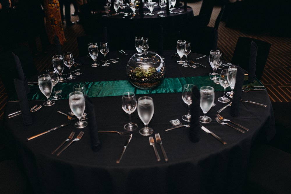  A table is set with a green satin runner and a succulent terrarium centerpiece.  