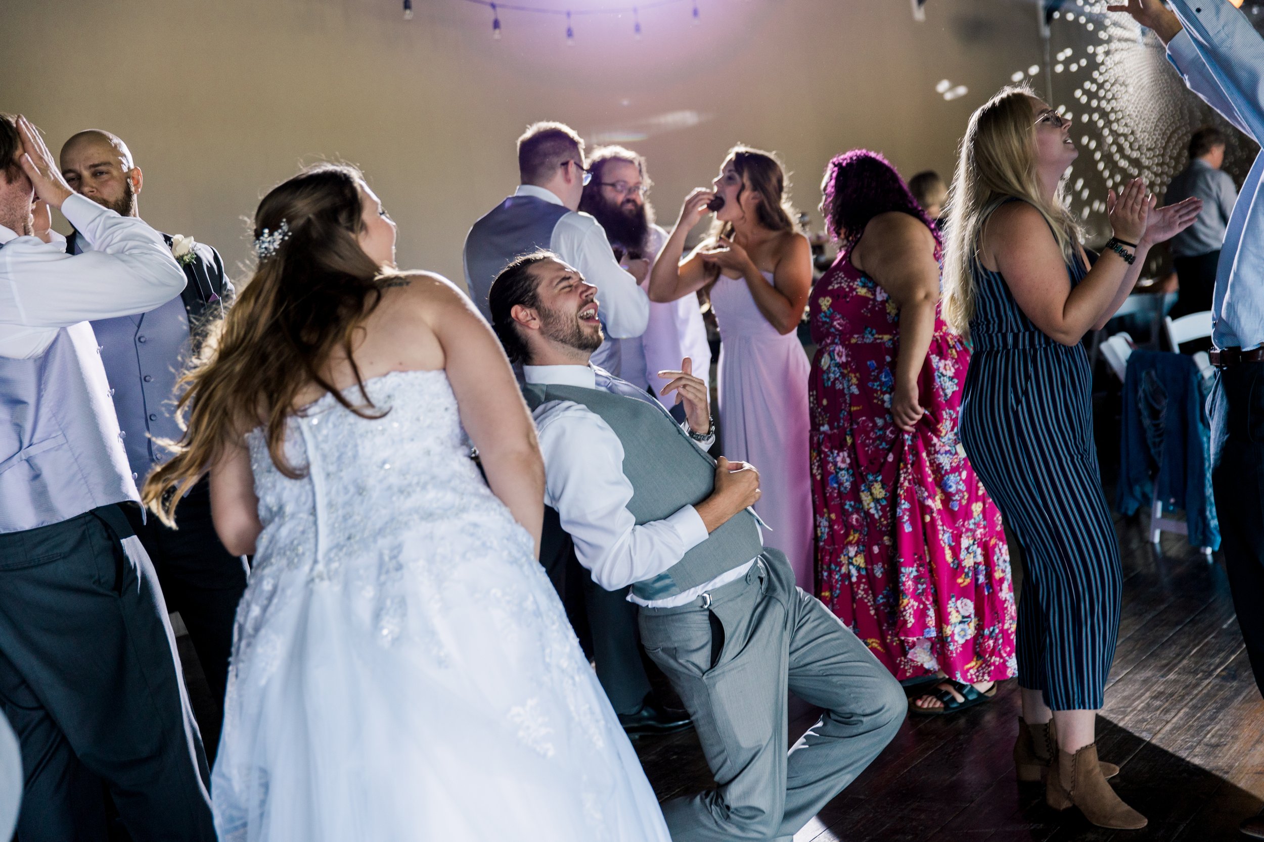  The dancefloor at a wedding reception. A person in the center of the frame plays air guitar. 