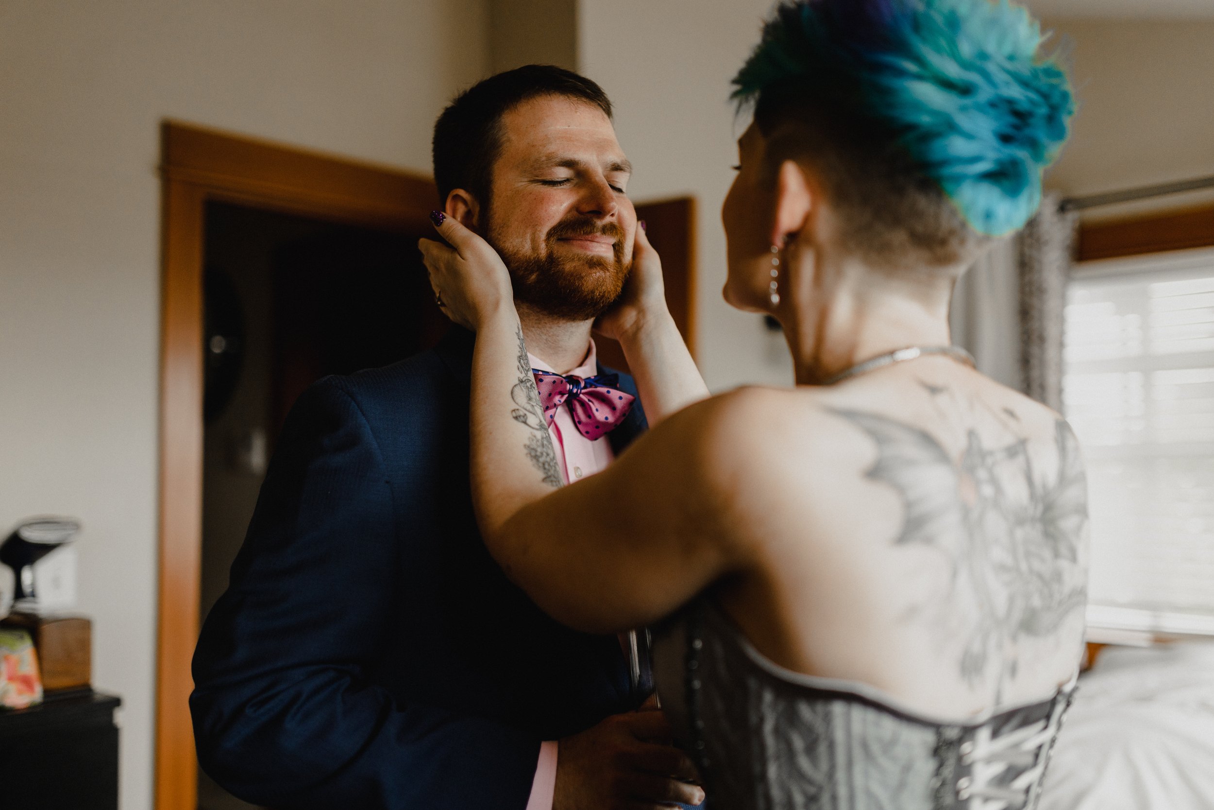  A groom is smiling facing his future spouse who has their hands cupped around his face. 