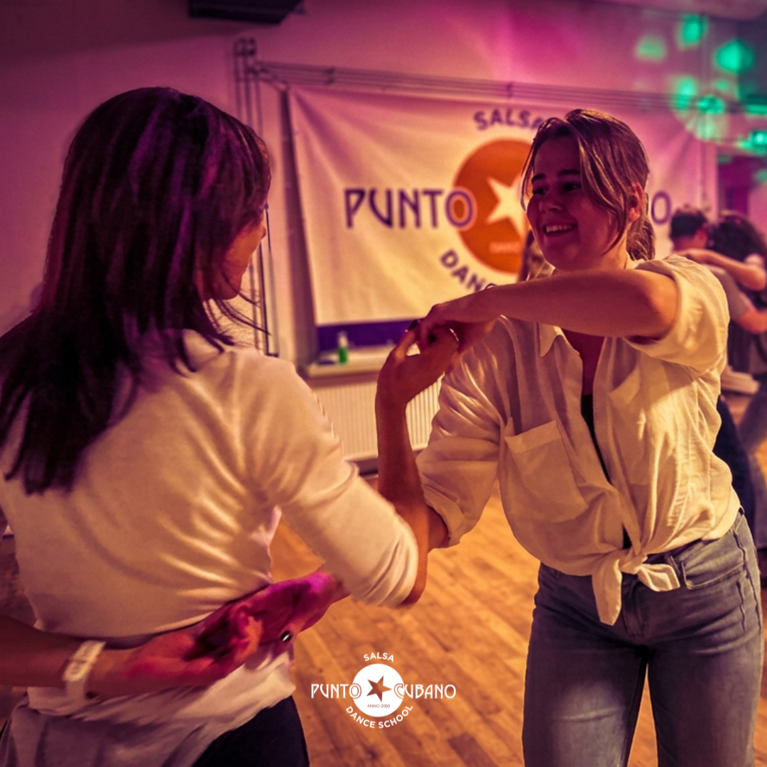 People dancing in a dance studio with a sign that says 'Start Course', indicating the beginning of a salsa dance class or workshop.