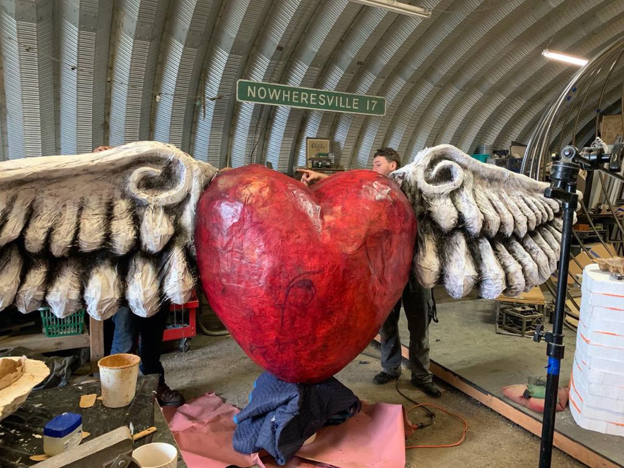 Artists work on a twenty foot winged heart sculpture inside a fabrication barn.