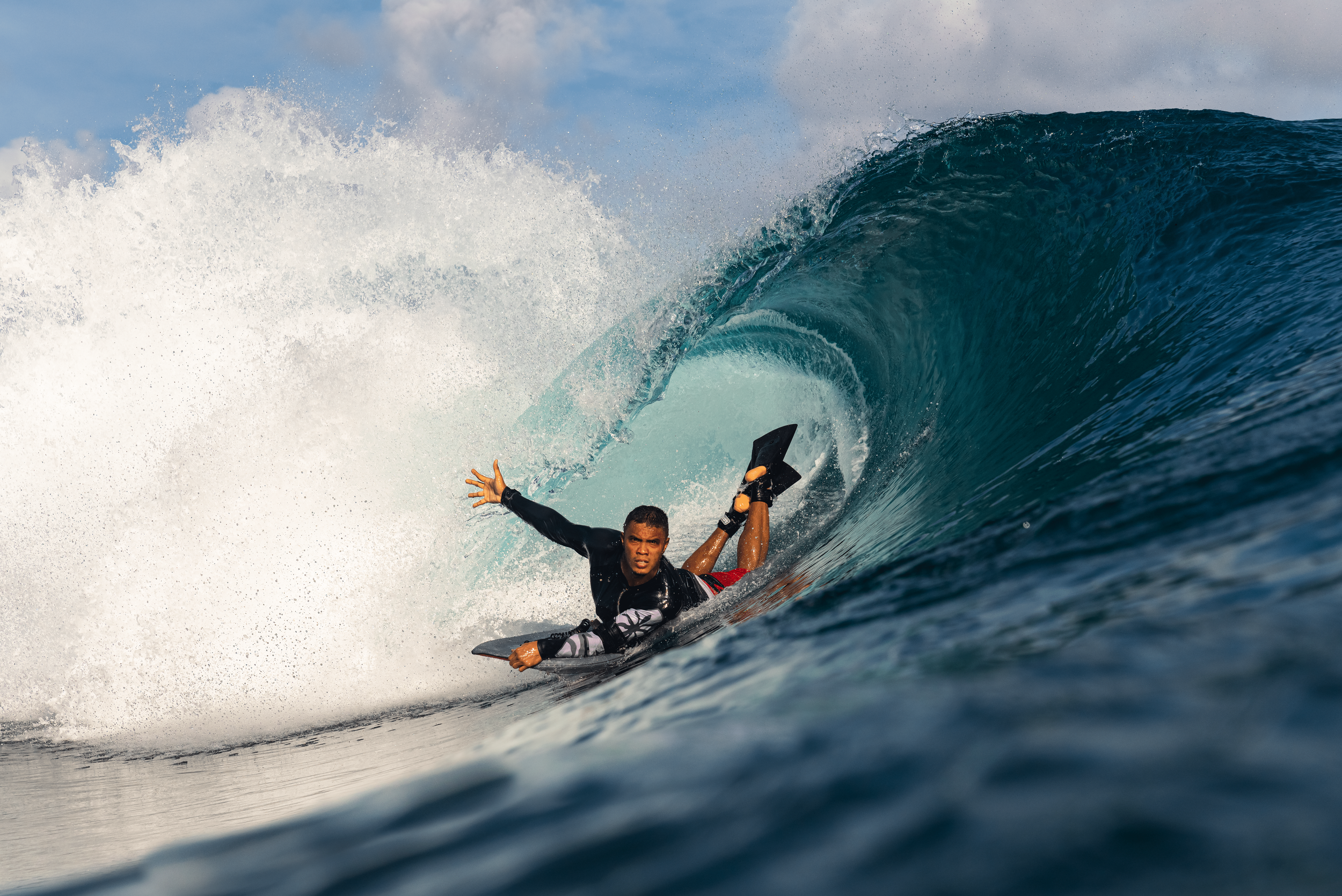 Surfer riding inside a large wave in the ocean with spray and blue sky.