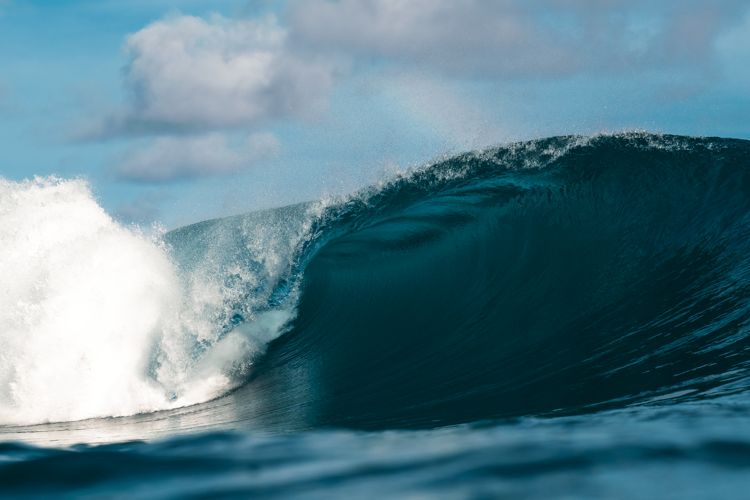 A large ocean wave breaking with surf and blue sky.
