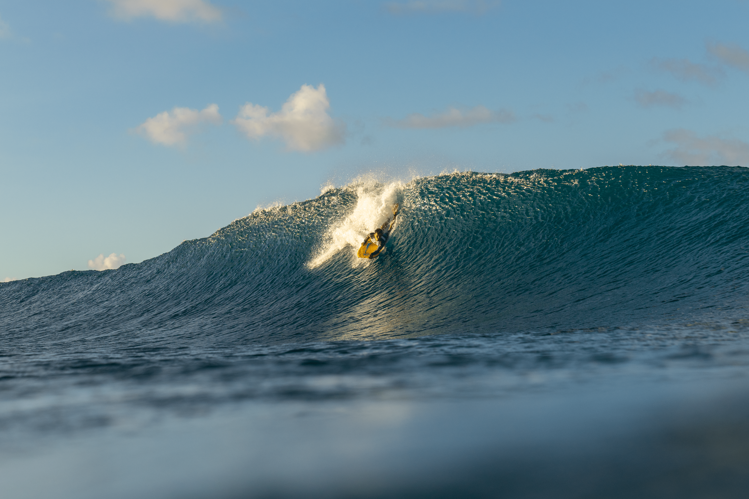 A surfer riding a large wave in the ocean with a partly cloudy sky in the background.