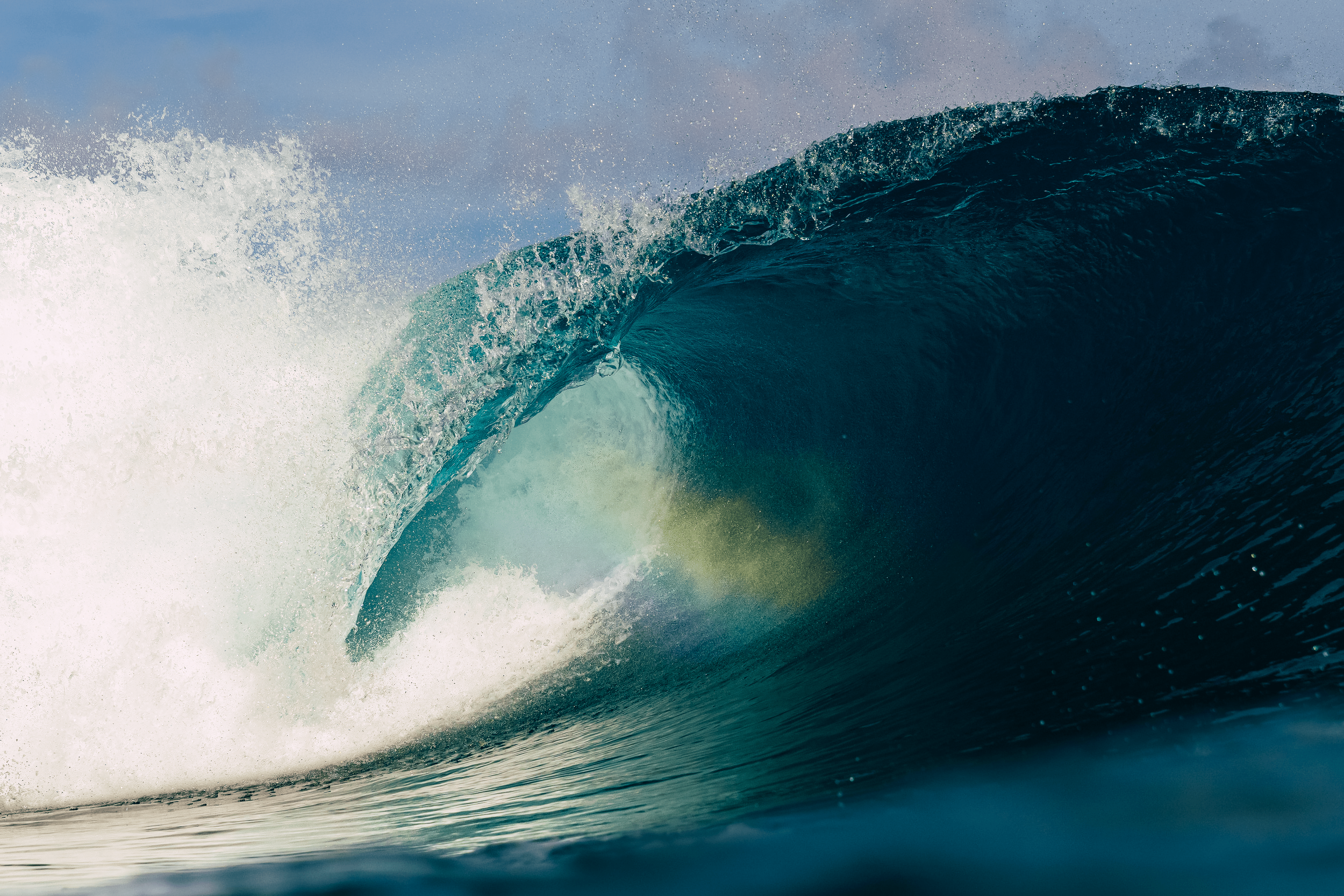 A large ocean wave curling and crashing, with white foam and spray in the air.