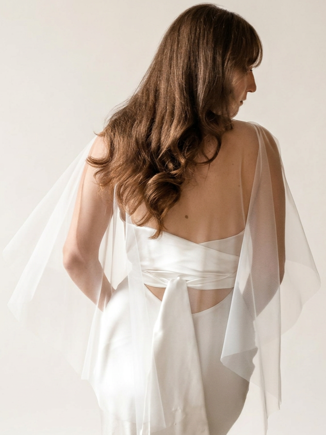 The back of a bride in a soft ivory tulle wedding shawl accessory
