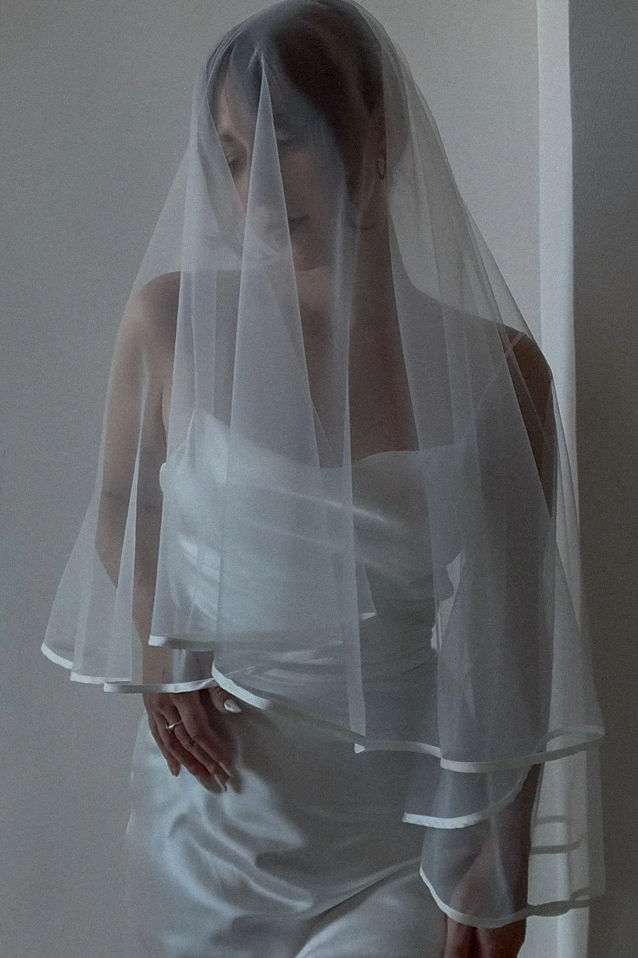 A bride wearing a two-tiered wedding veil with a blusher that is trimmed in an ivory satin bias binding (Copy)
