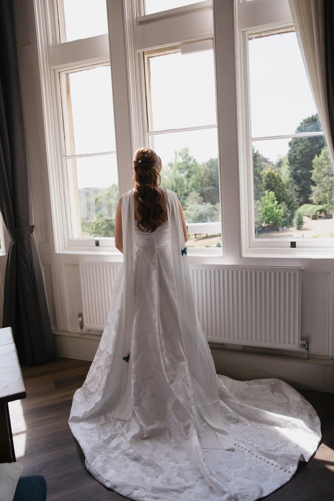 Bride standing by a window with two blue butterfly accessories attached to her neck scarf