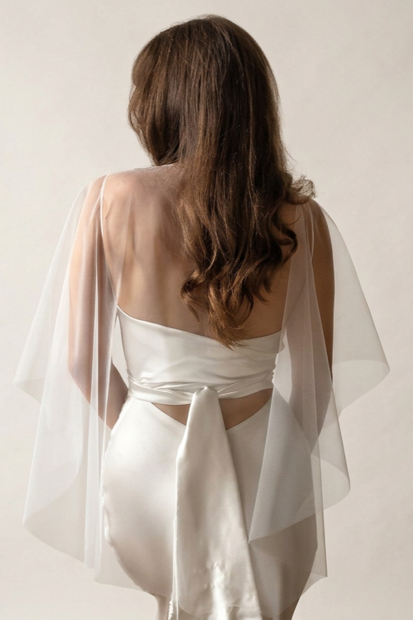 the back of a bride who is wearing a delicate off-white wedding cape