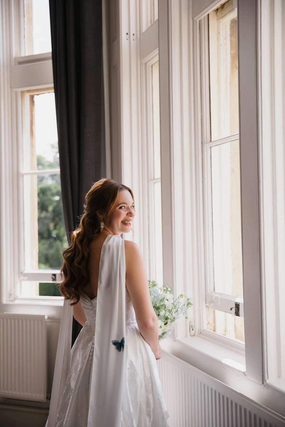 Bride standing by a window with a neck scarf and butterfly magnets.
